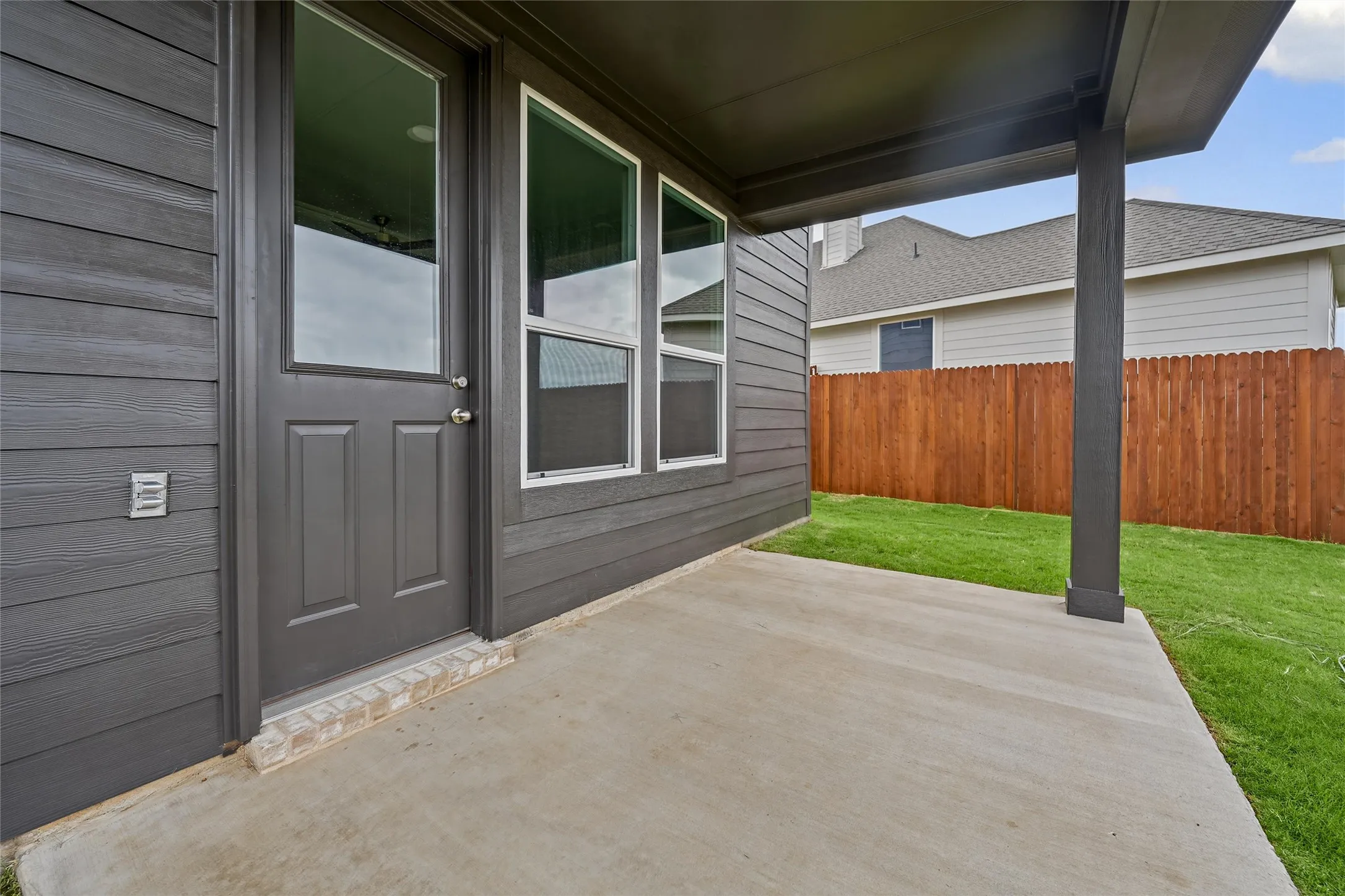 Covered concrete patio with a full-light panel door, adjacent windows, and wood panel fencing