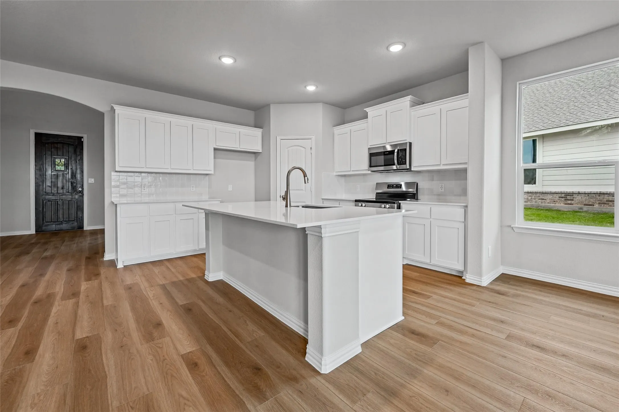 Kitchen featuring wood-finish flooring, white cabinetry, a central island with an integrated sink, stainless steel appliances, and recessed lighting