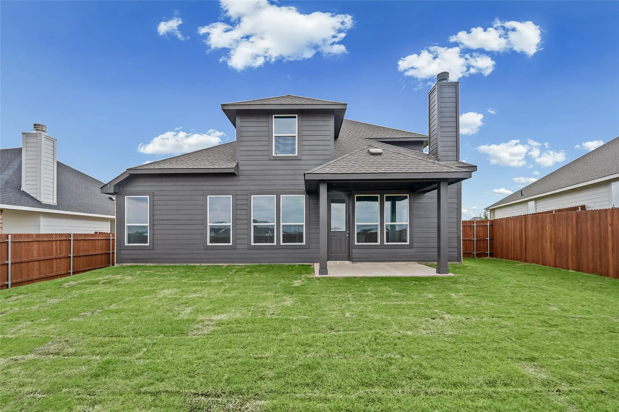 Expansive backyard with a covered patio, multiple windows, and a wood privacy fence