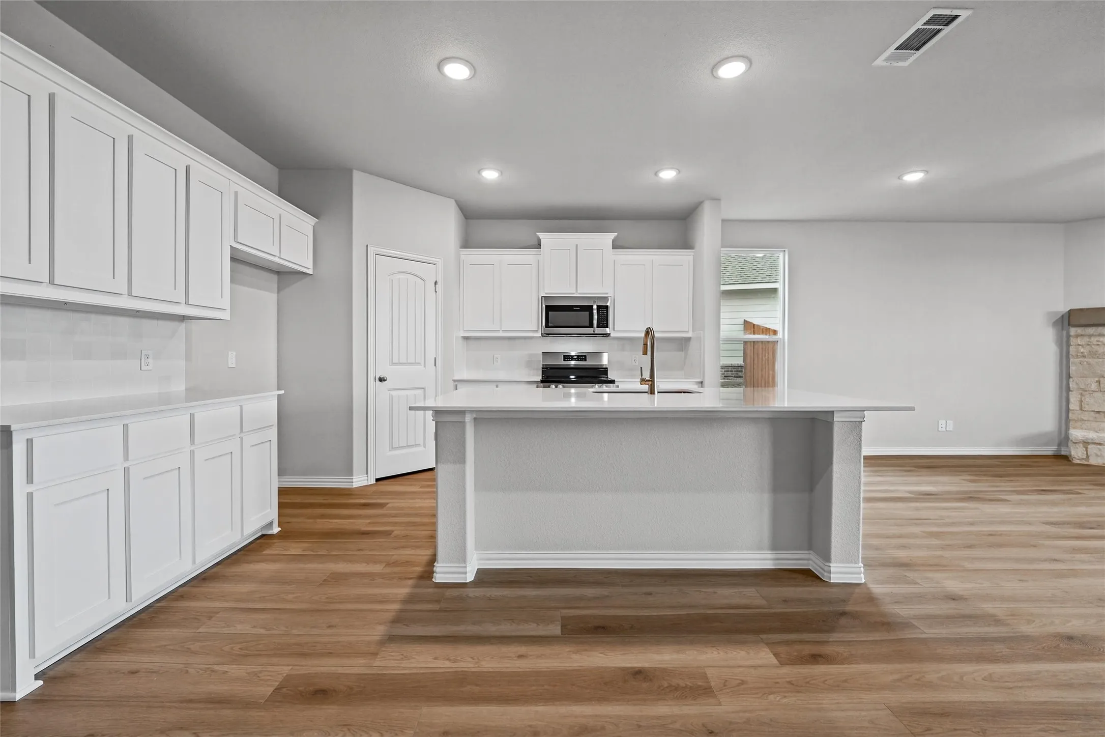 Kitchen featuring an island with a built-in sink, white cabinetry, integrated appliances, recessed lighting, and wood-finish flooring