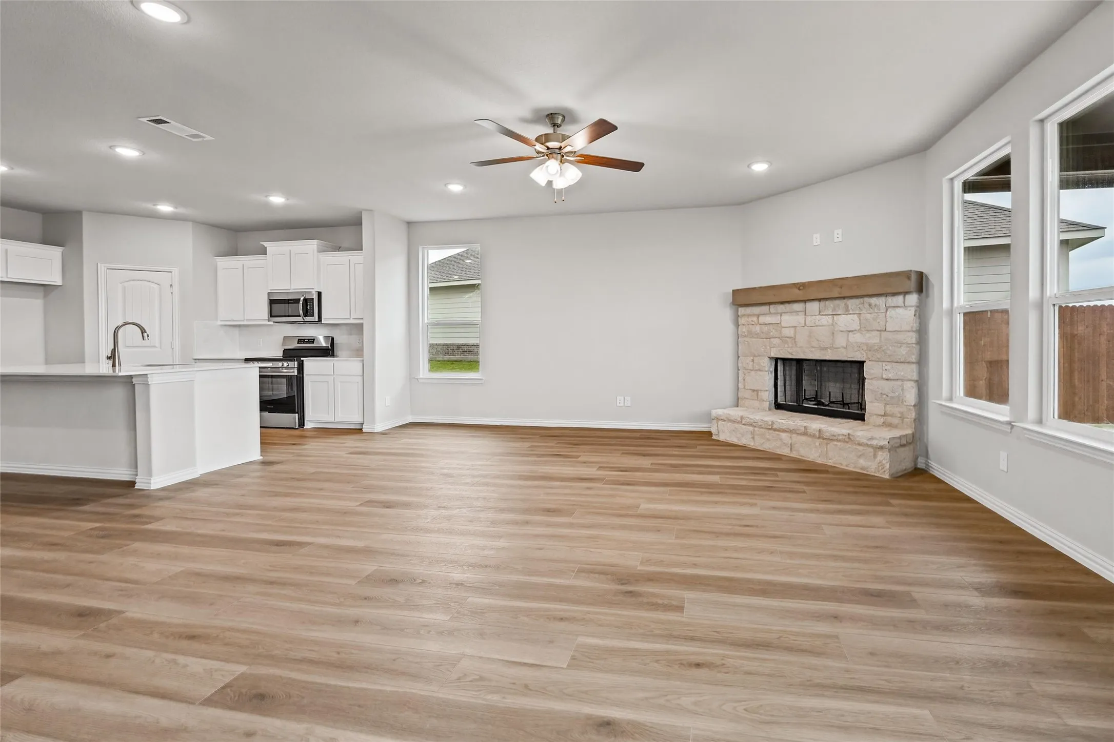 Open-concept living area featuring wood-finish flooring, a stone fireplace with a wood mantle, recessed lighting, and multiple windows