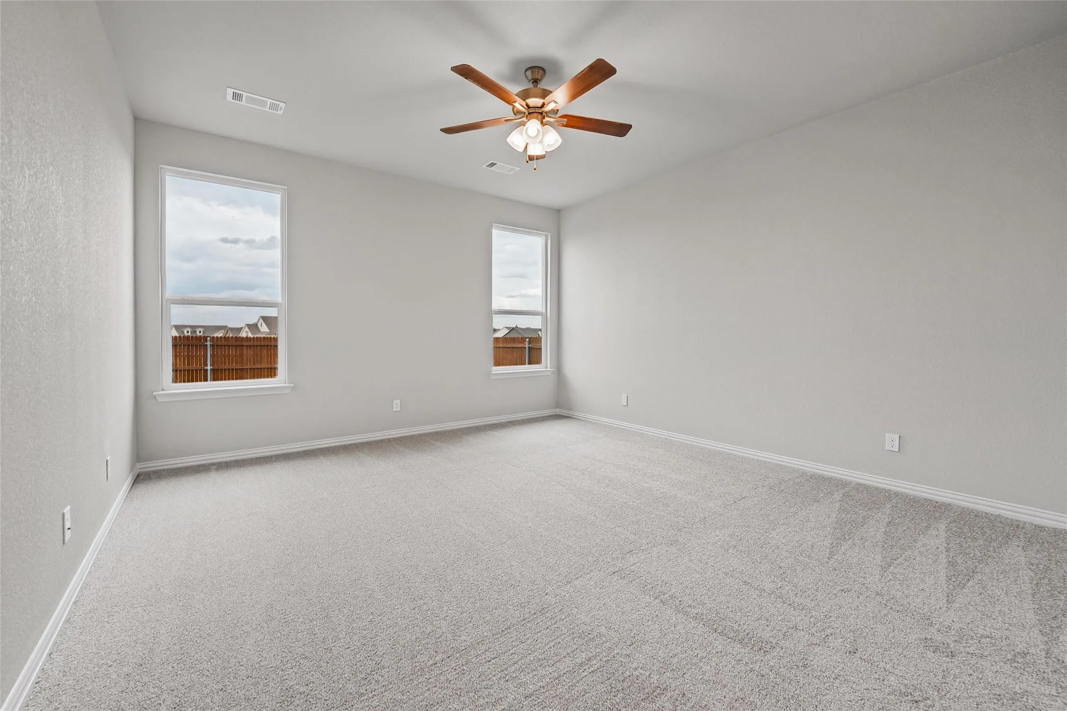 Spacious room featuring neutral carpeting, light-toned walls, two windows with white trim, and a ceiling fan with light fixture