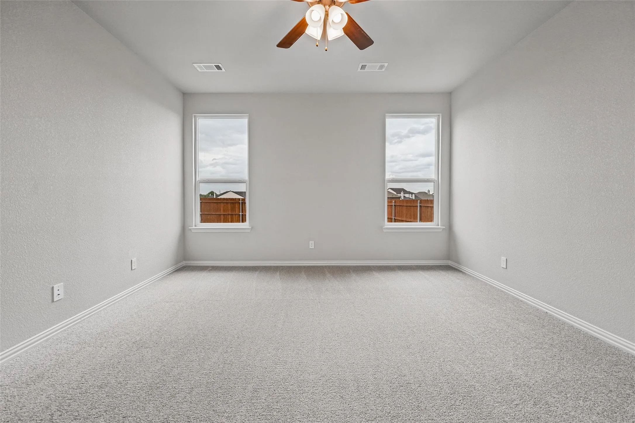 Carpeted flooring, two windows, ceiling fan with light fixture, and light-toned walls
