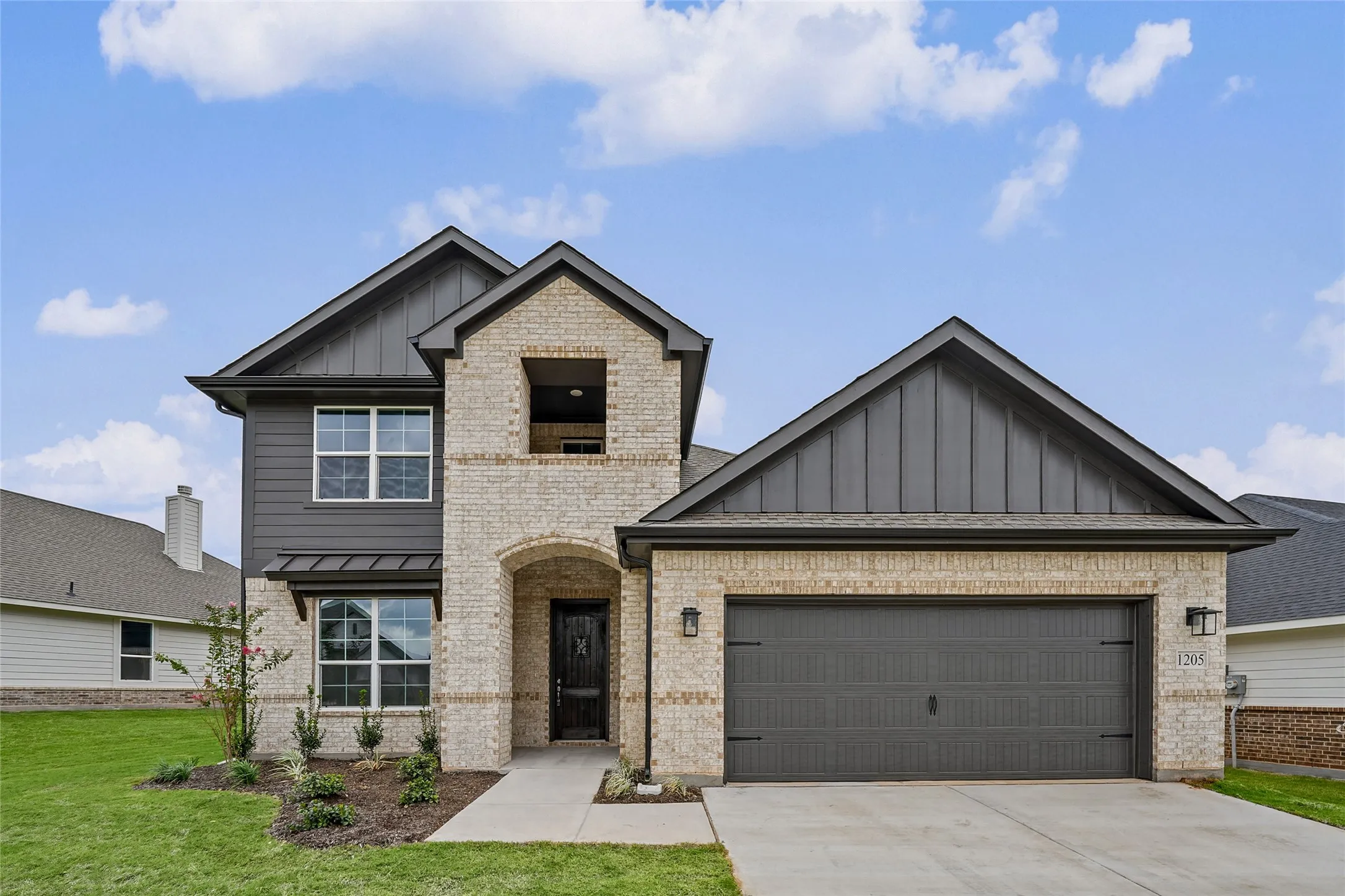 Two-story exterior with a two-car garage, brick facade, board and batten siding, and architectural shingles