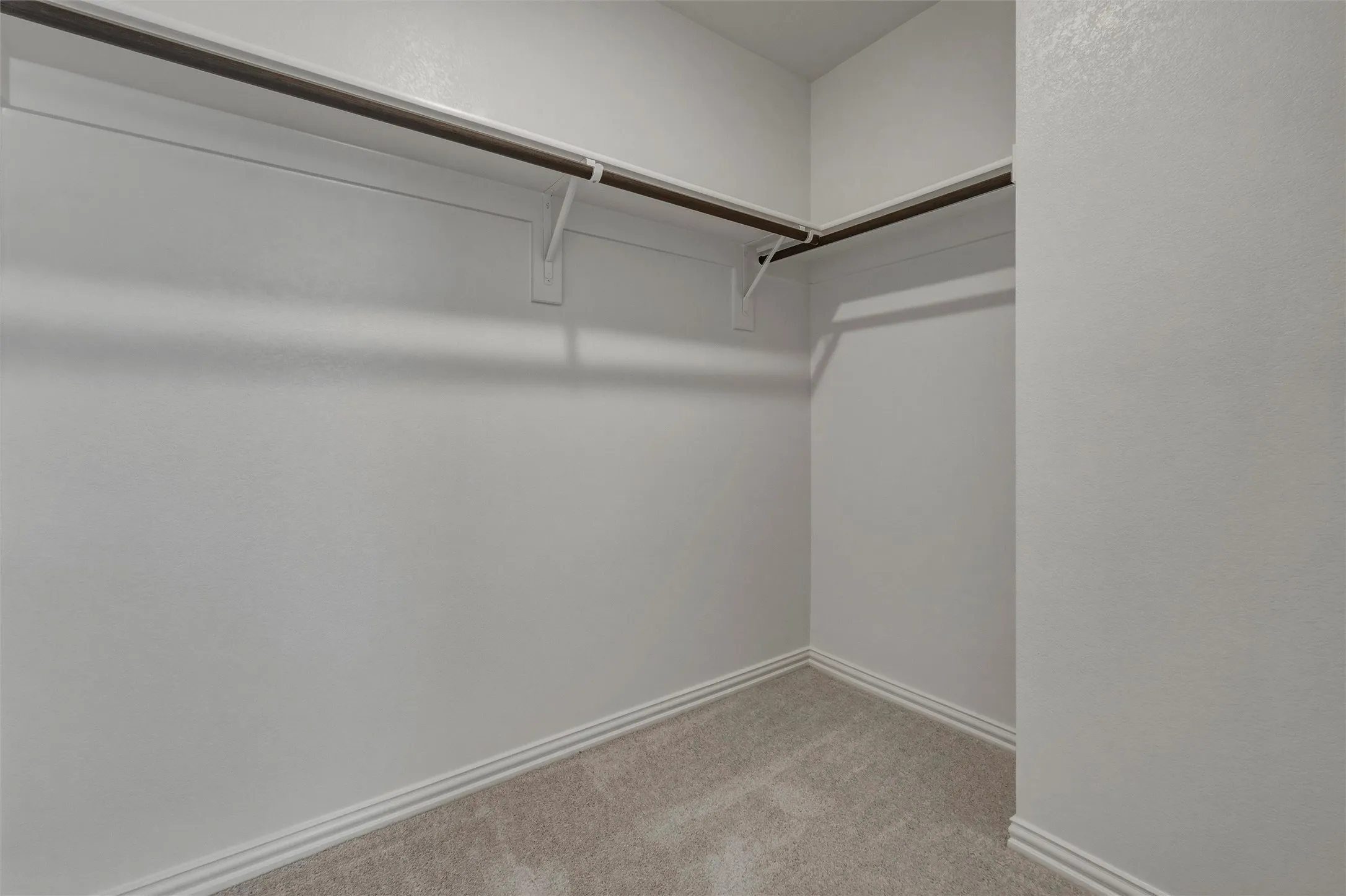 Spacious walk-in closet with dual hanging rods, carpeted flooring, and white painted walls with crown molding detail