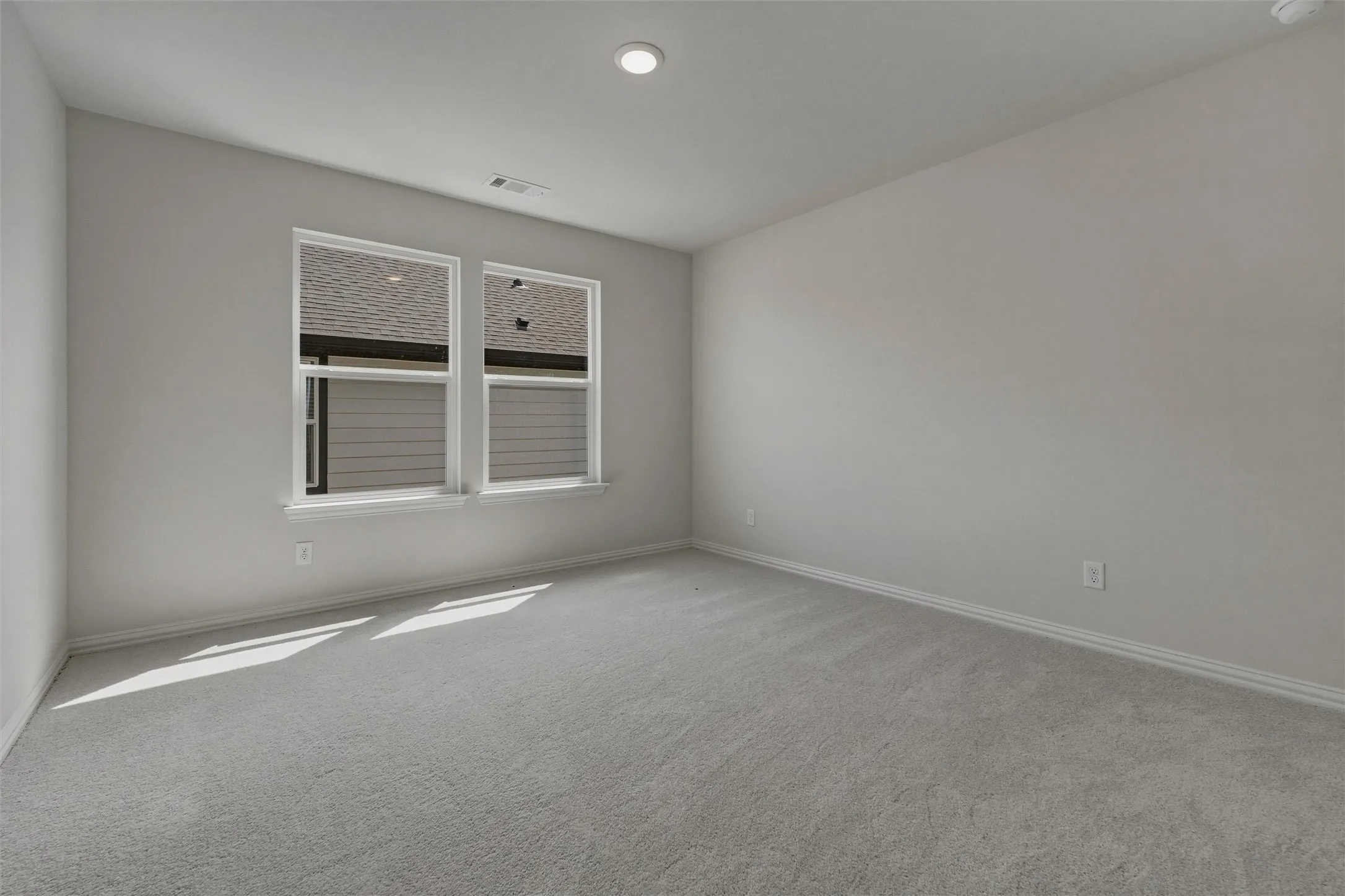 Recessed ceiling light, two windows with white trim, light gray wall paint, and gray carpet flooring