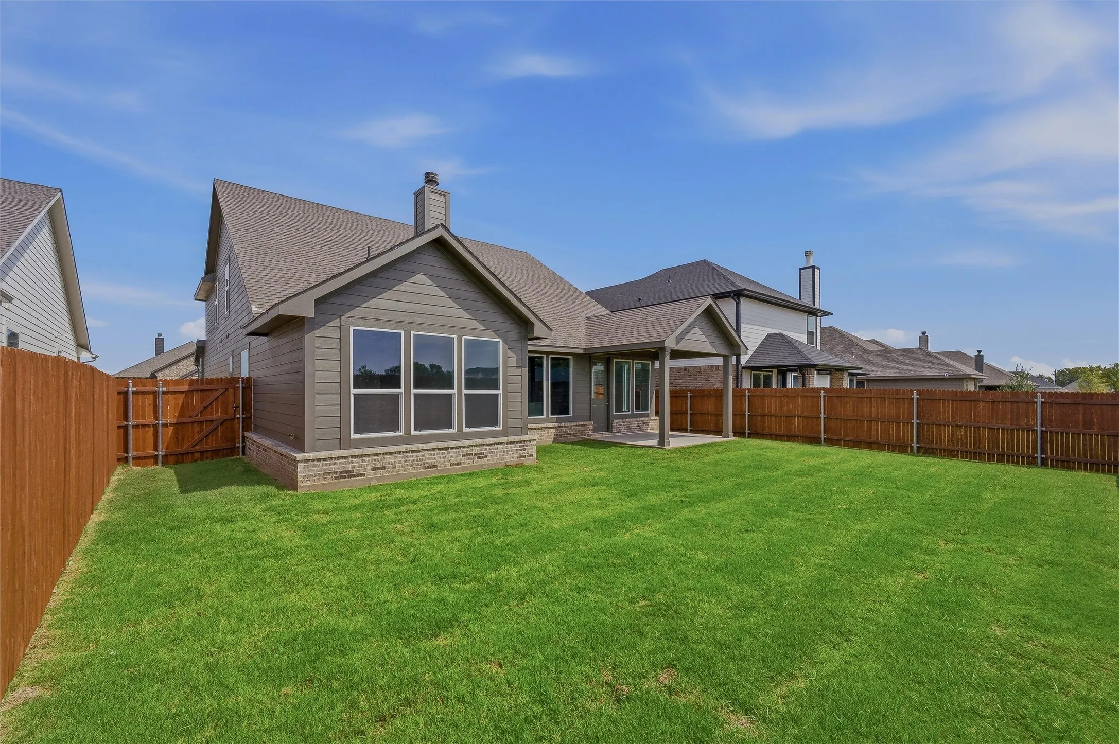 Expansive backyard with a manicured lawn, full privacy fencing, and a covered patio