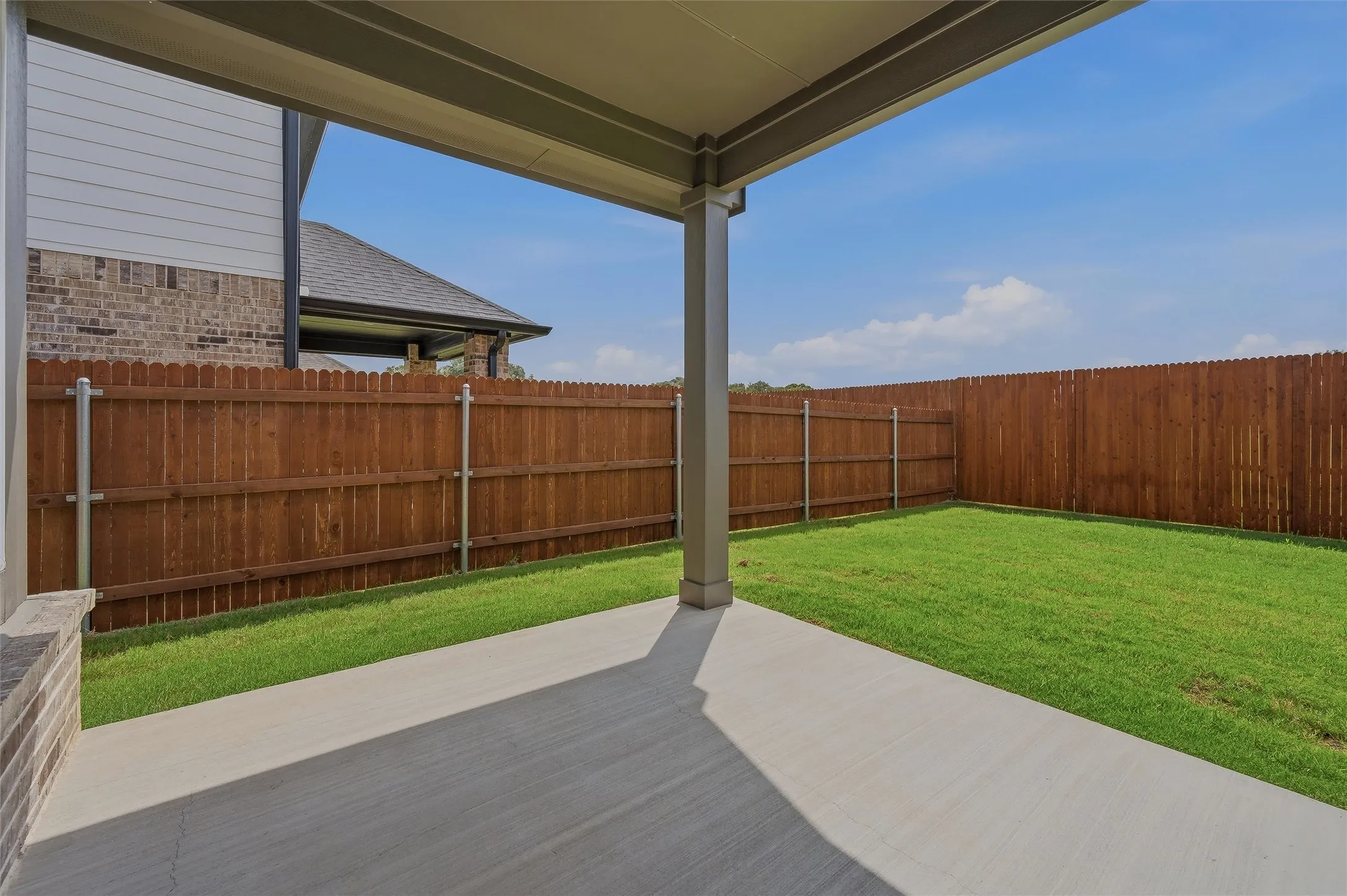 Covered patio with a concrete surface, expansive lawn, and wood-paneled fencing