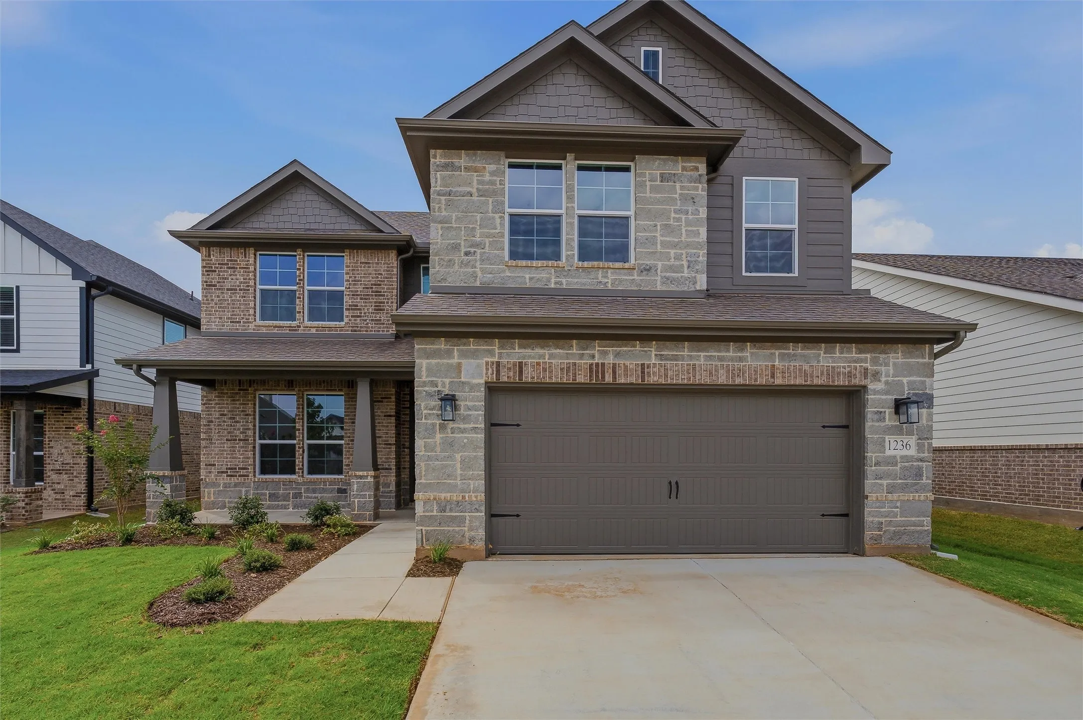 Stone and brick facade with a covered entry, two-car garage, and established landscaping