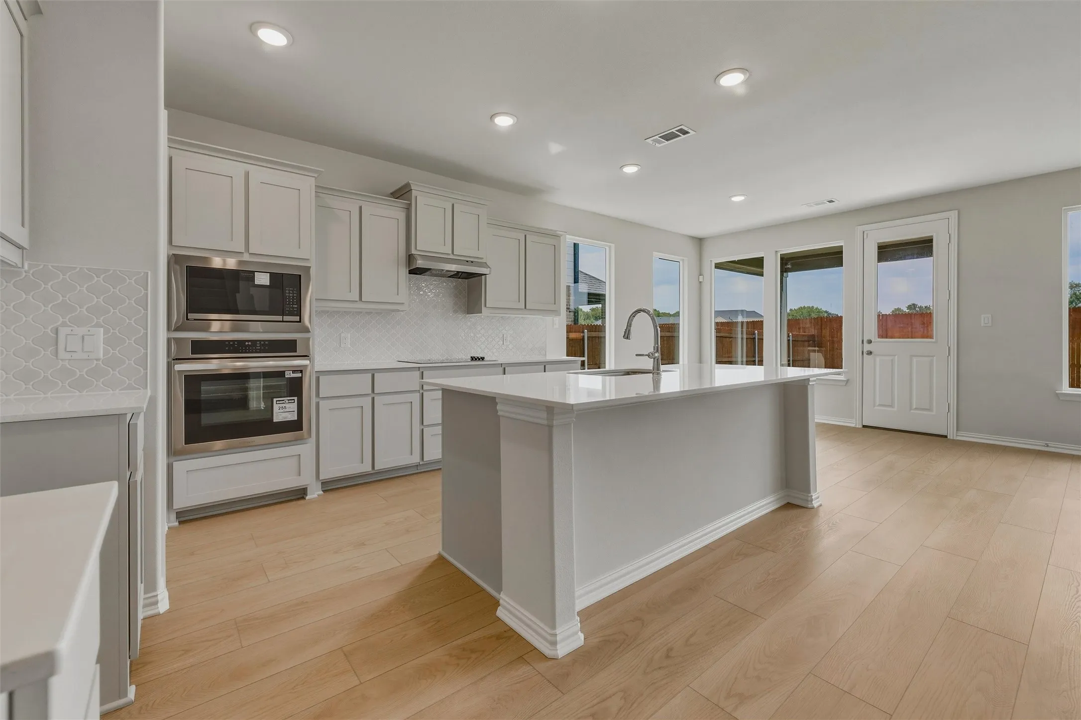 Open-concept kitchen featuring an expansive island with a stainless steel sink, light wood-finish flooring, white cabinetry, and stainless steel appliances