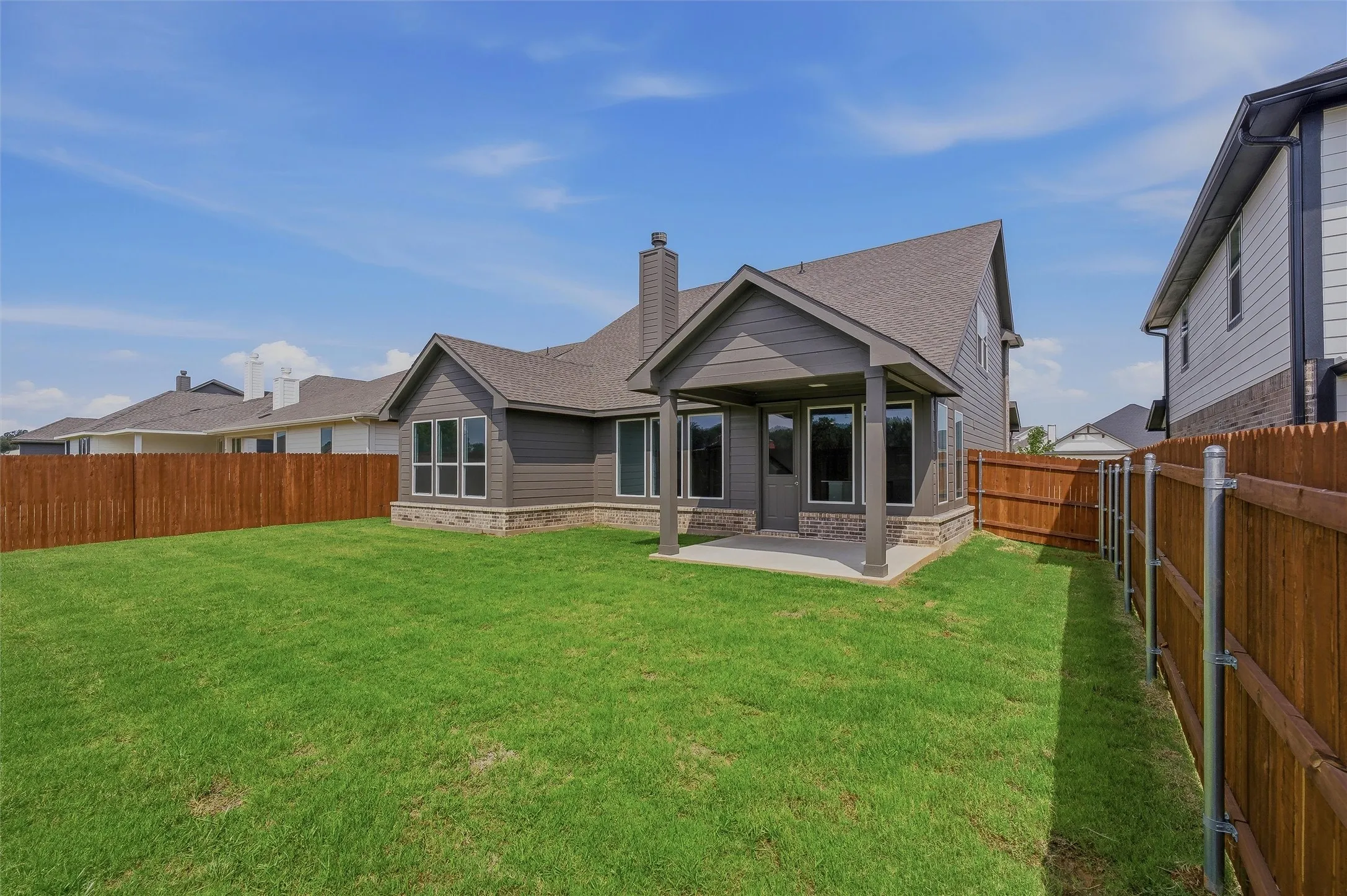 Expansive backyard with a manicured lawn, full wood fencing, and a covered patio with stone accents