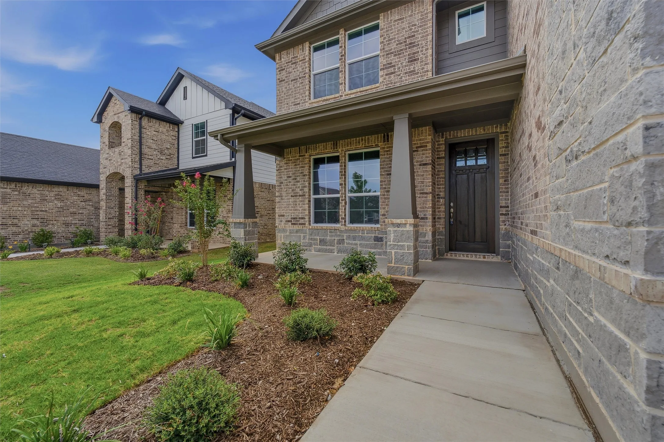 Brick and stone exterior with a covered entry, dark wood-paneled door with glass inserts, and concrete pathway