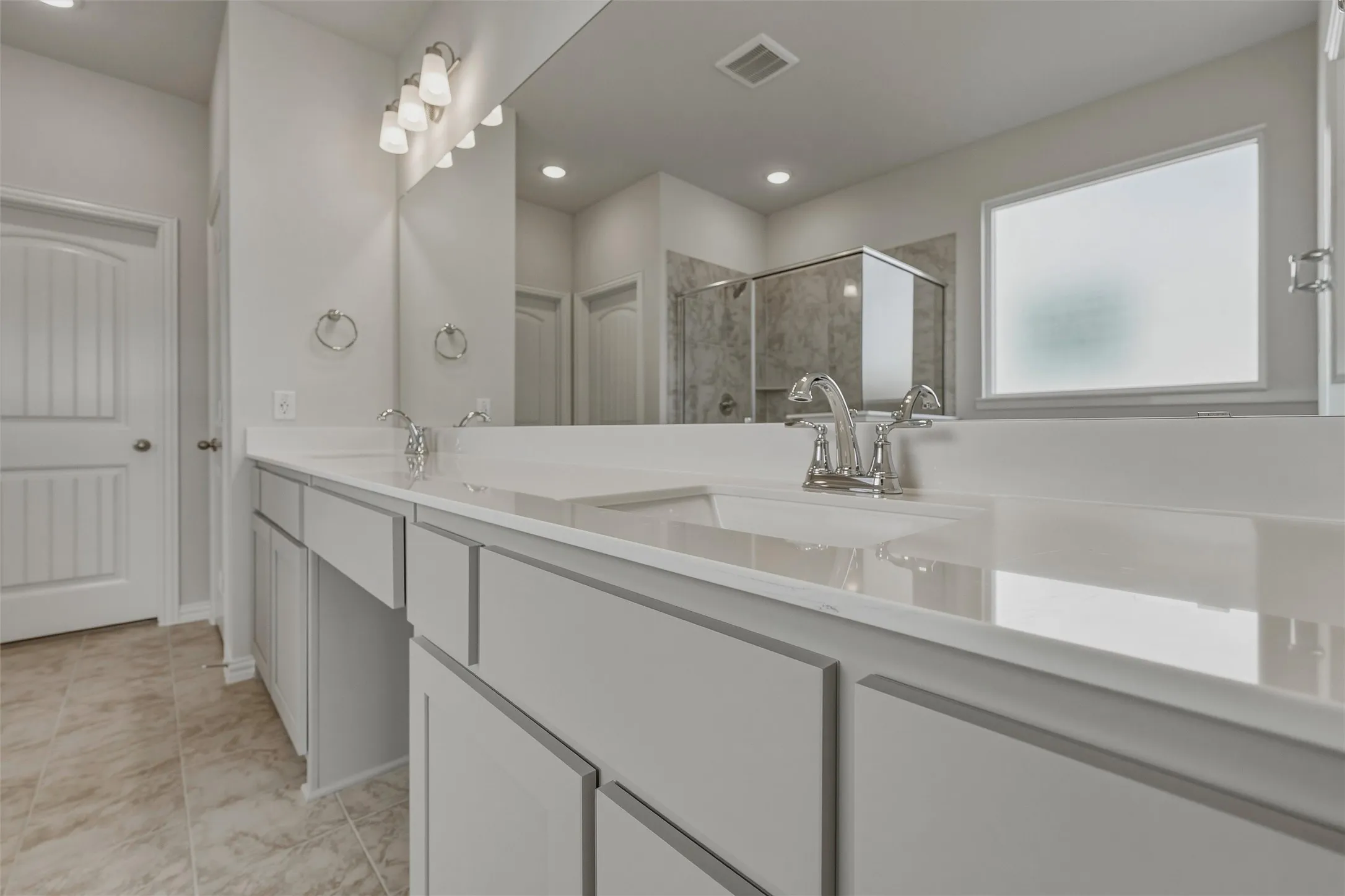 Dual sinks with chrome faucets, light gray cabinetry, and a large mirror
