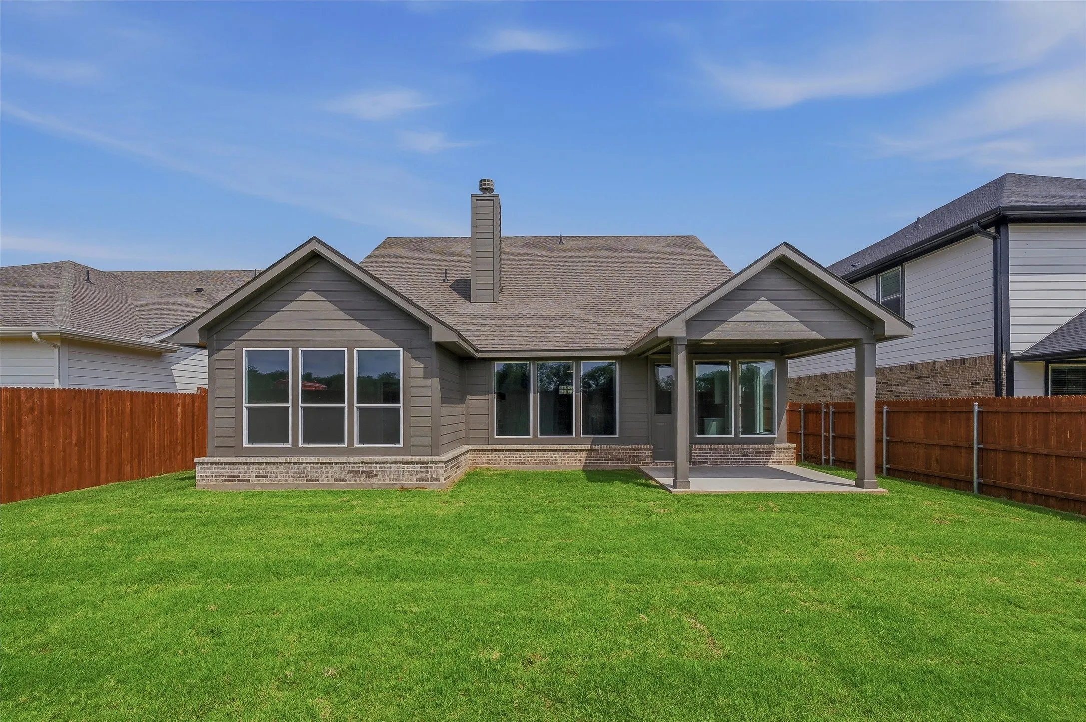 Expansive backyard featuring a covered patio, brick foundation, wood siding, and multiple windows