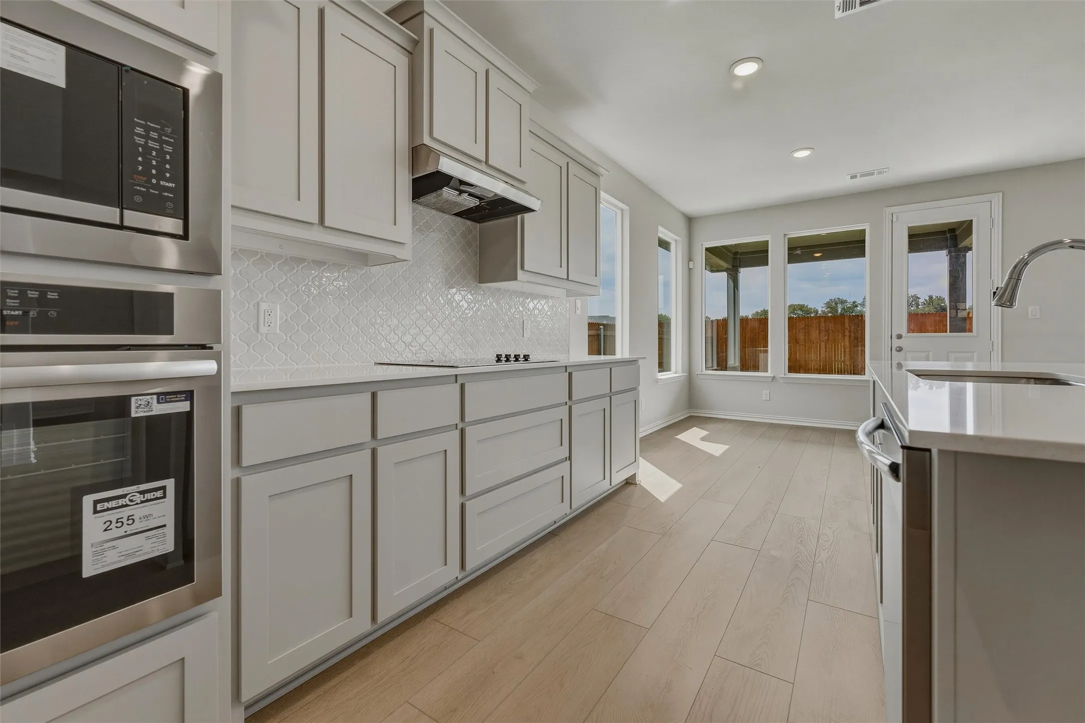 Kitchen featuring light-toned cabinetry, stainless steel appliances, a textured tile backsplash, solid surface countertops, and wood-finish flooring