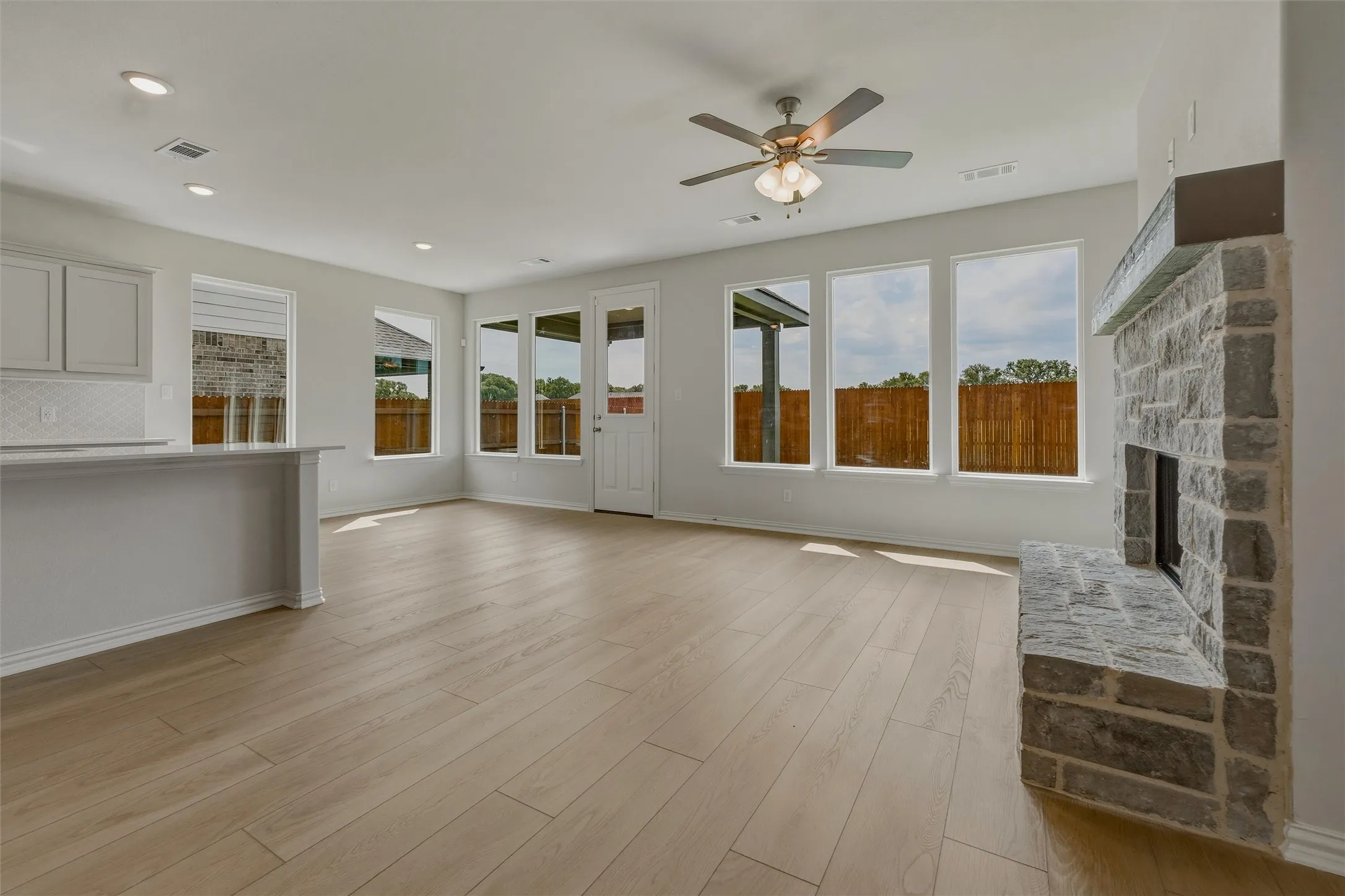 Light wood-finish flooring, recessed lighting, and a stone-clad fireplace with a hearth