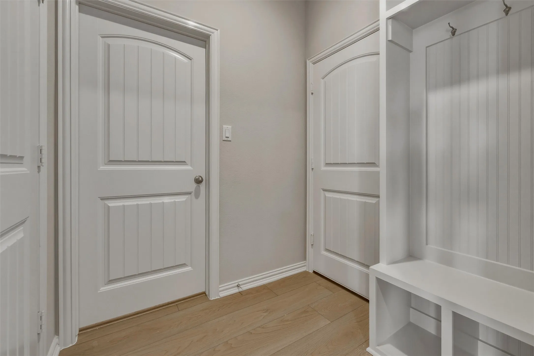 Light wood-finish flooring, built-in storage with beadboard paneling, and paneled interior doors