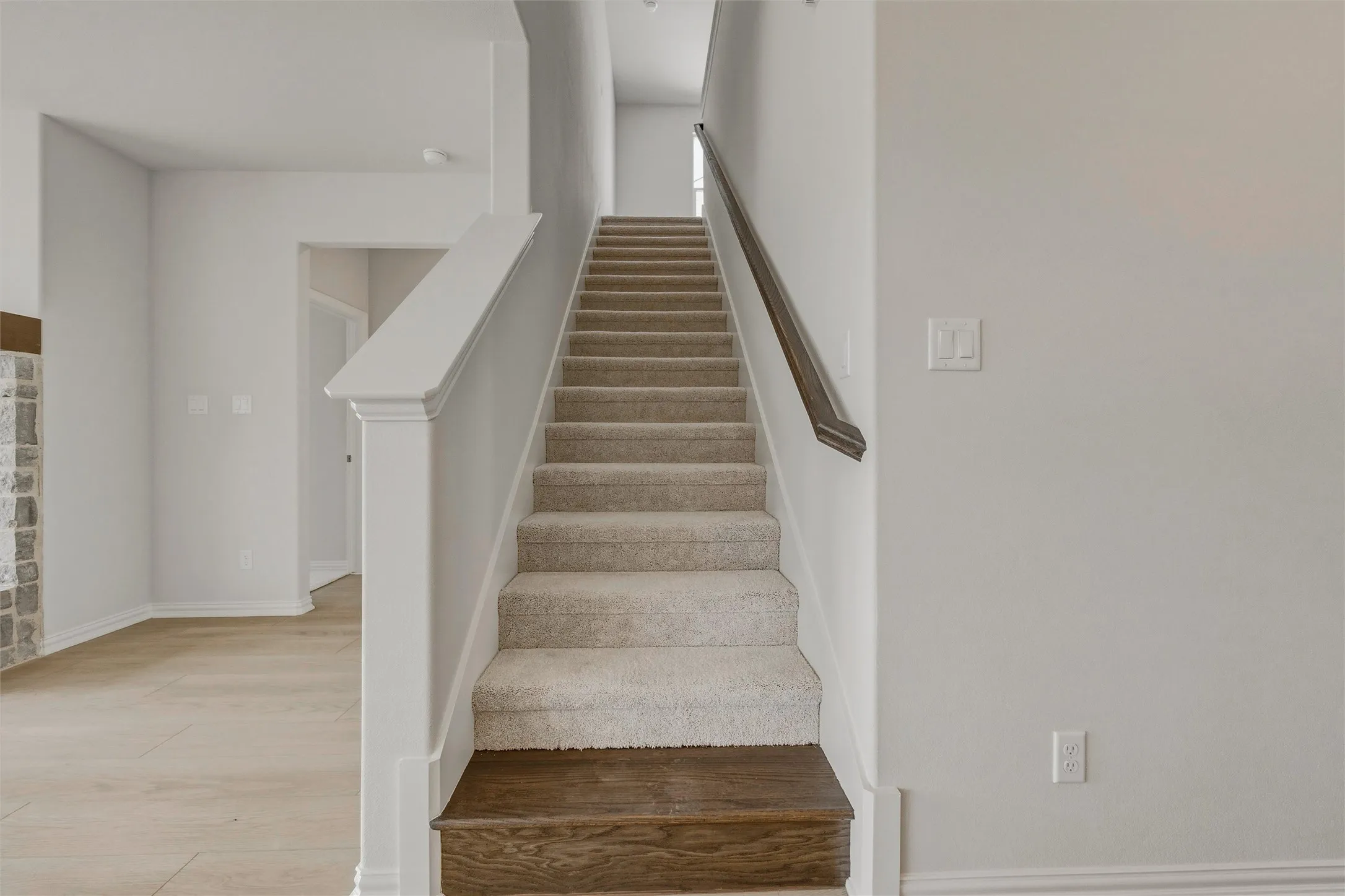 Carpeted staircase with dark wood-finish treads and handrail, crisp white newel post, and light wood-finish flooring