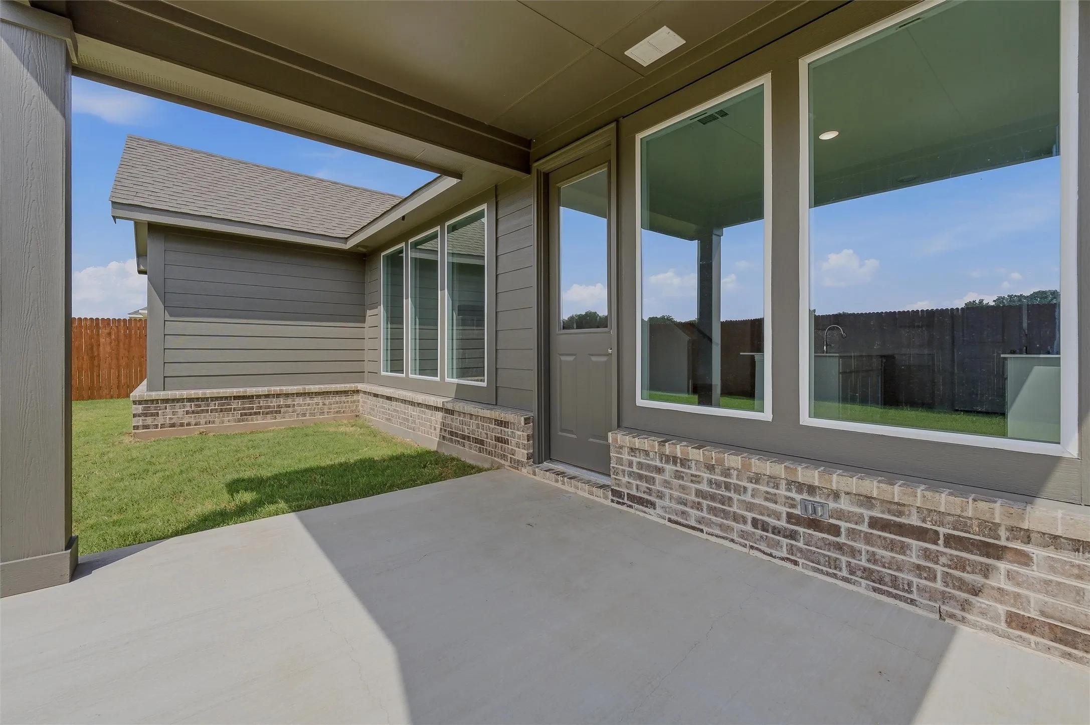 Covered patio with concrete flooring, brick wainscoting, large windows, and a solid exterior door
