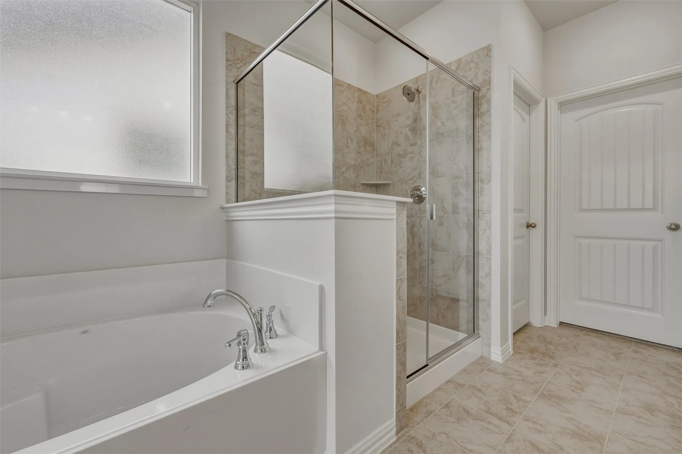 Built-in soaking tub with chrome fixtures, glass-enclosed shower with tile surround, and frosted window