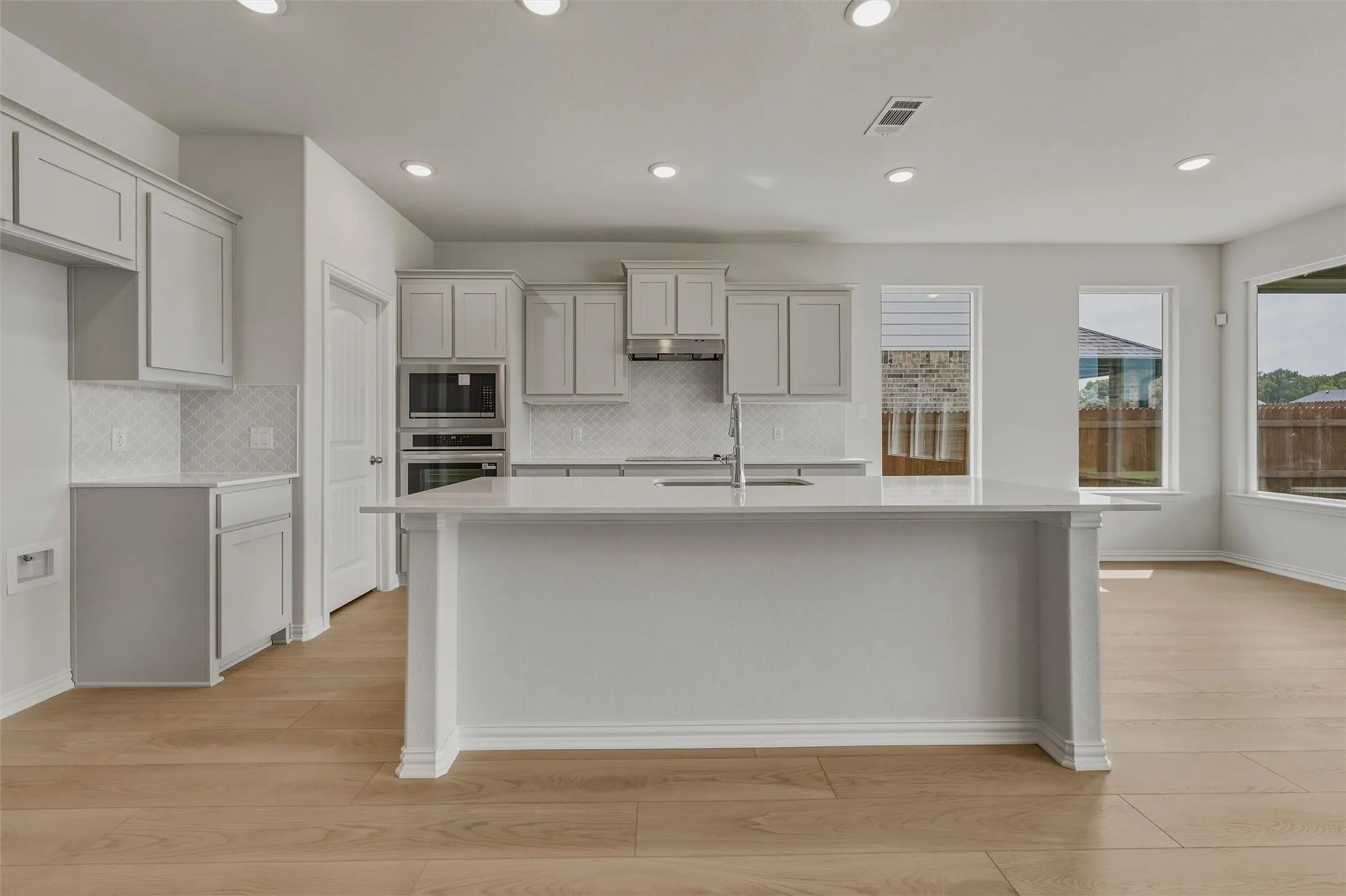 Modern kitchen featuring recessed lighting, light-toned cabinetry, light-toned countertops, a light-toned kitchen island, and wood-finish flooring