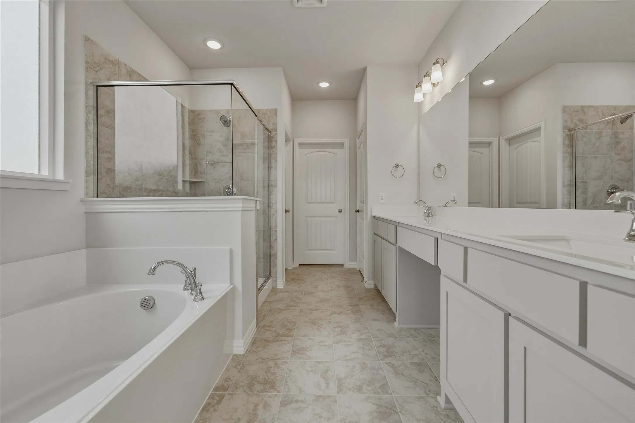 Spacious bathroom featuring a built-in soaking tub, a walk-in shower with glass enclosure, a dual vanity with ample counter space, and light-toned floor tiling