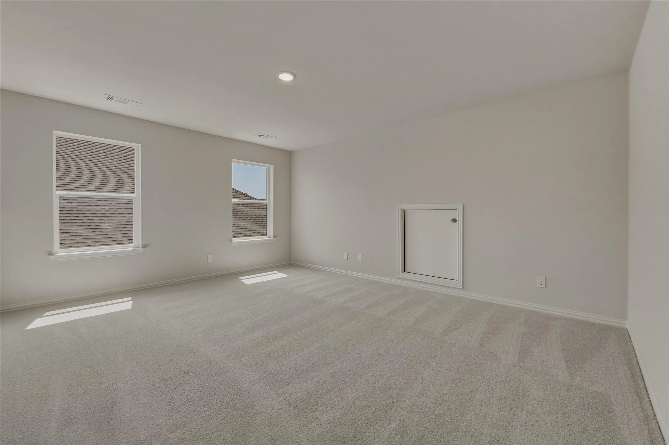 Neutral-toned wall paint, recessed ceiling lighting, light-colored carpeting, two windows, and a wall access panel