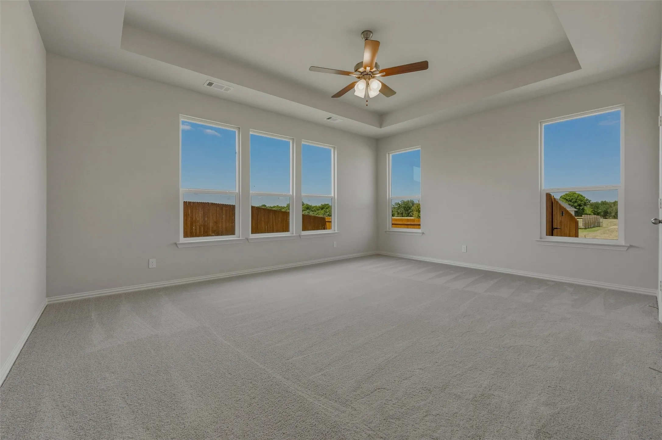 Spacious room featuring a tray ceiling, ceiling fan, and carpeted flooring
