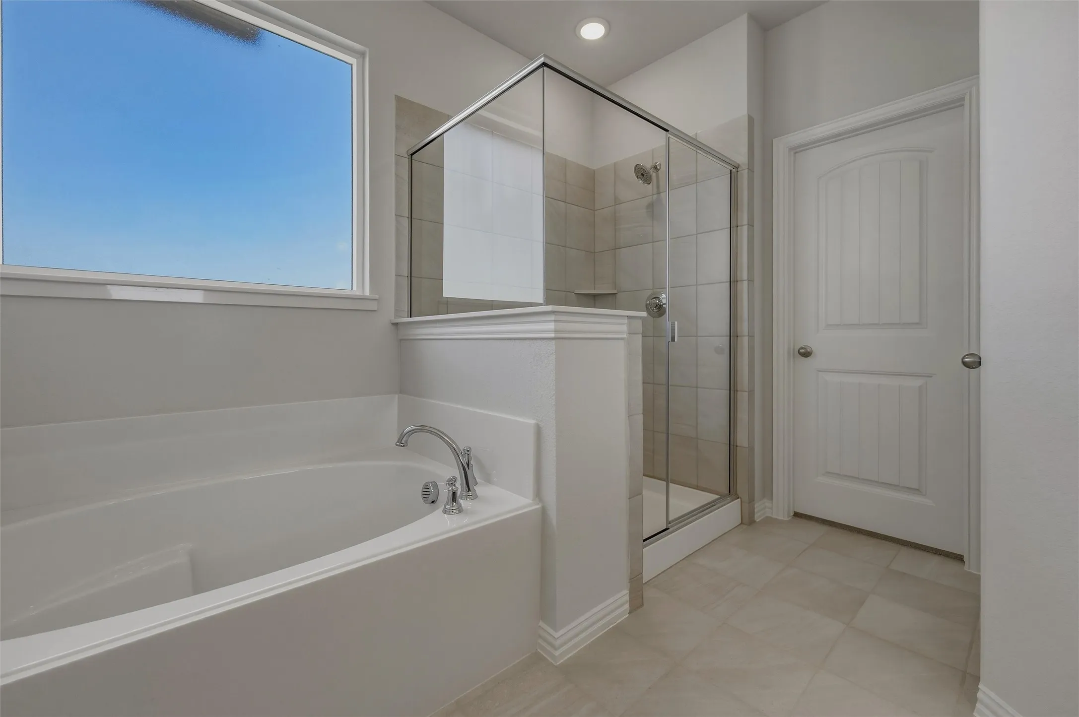 Soaking tub with chrome fixtures, glass-enclosed shower with tiled surround, large window, and tiled flooring