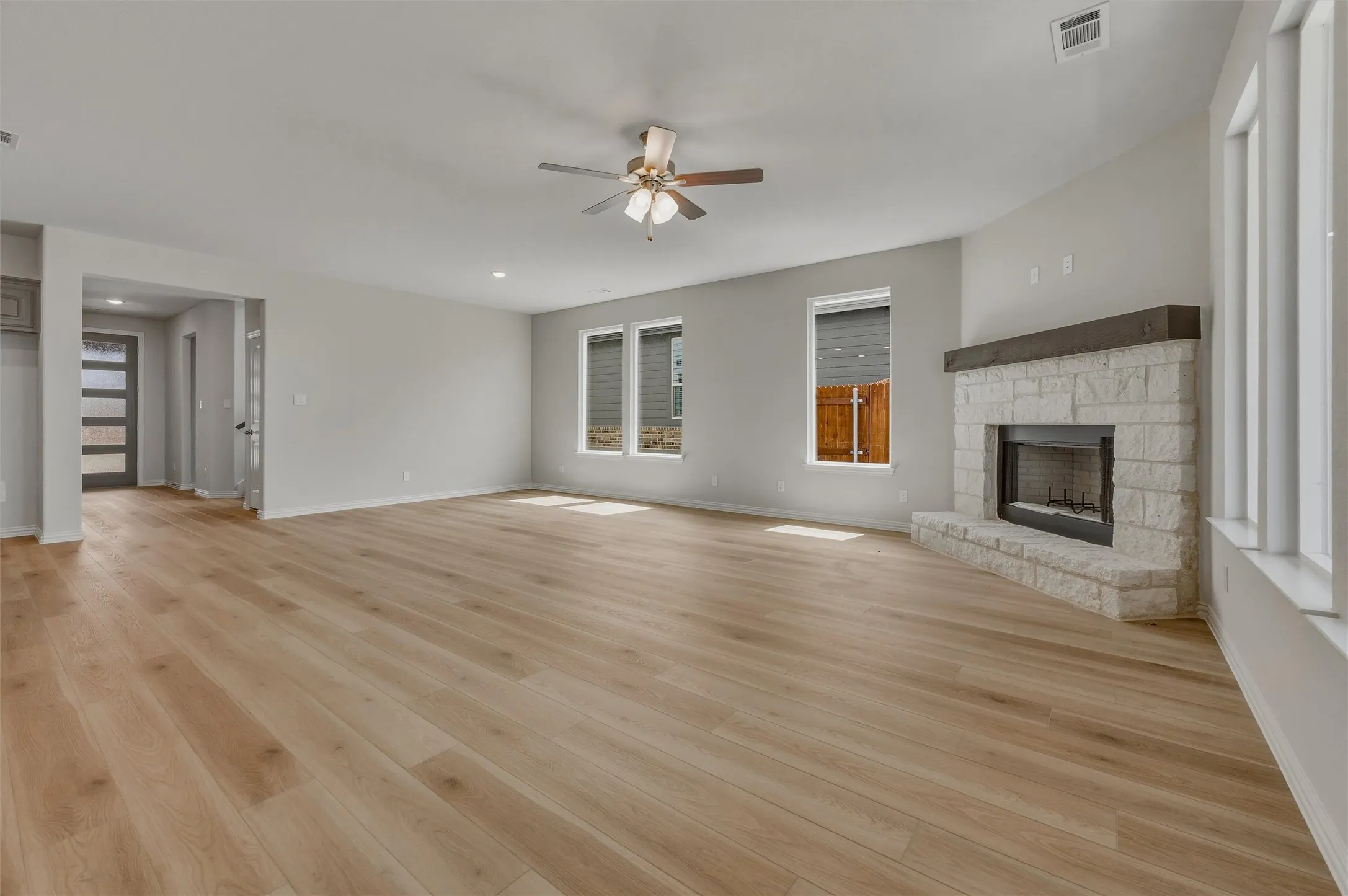 Spacious interior with wood-finish flooring, stone-clad fireplace with wood mantle, and ceiling fan