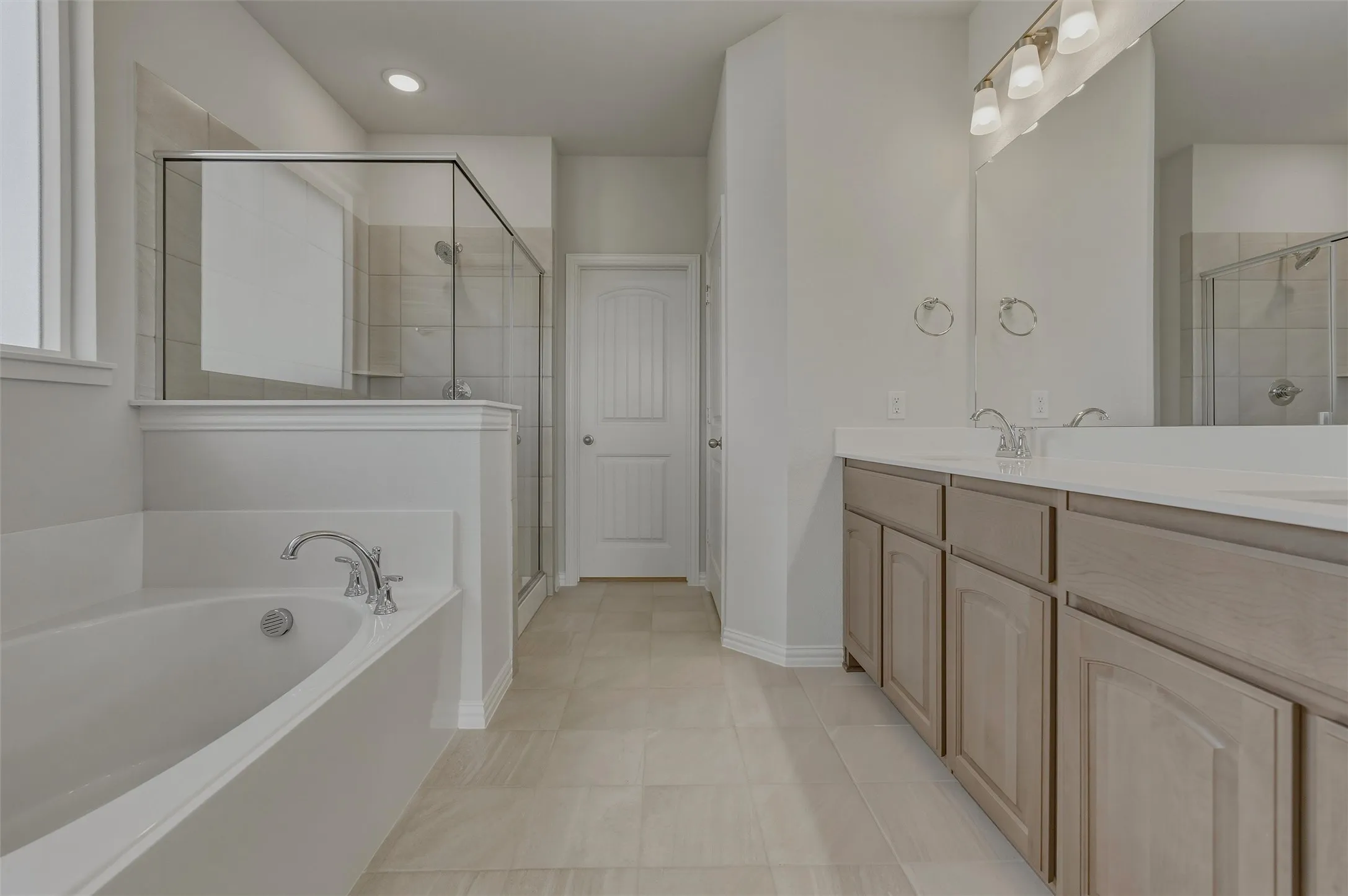 Dual vanity with light-tone cabinetry and white countertop, recessed lighting, chrome fixtures, soaking tub, and a glass-enclosed shower