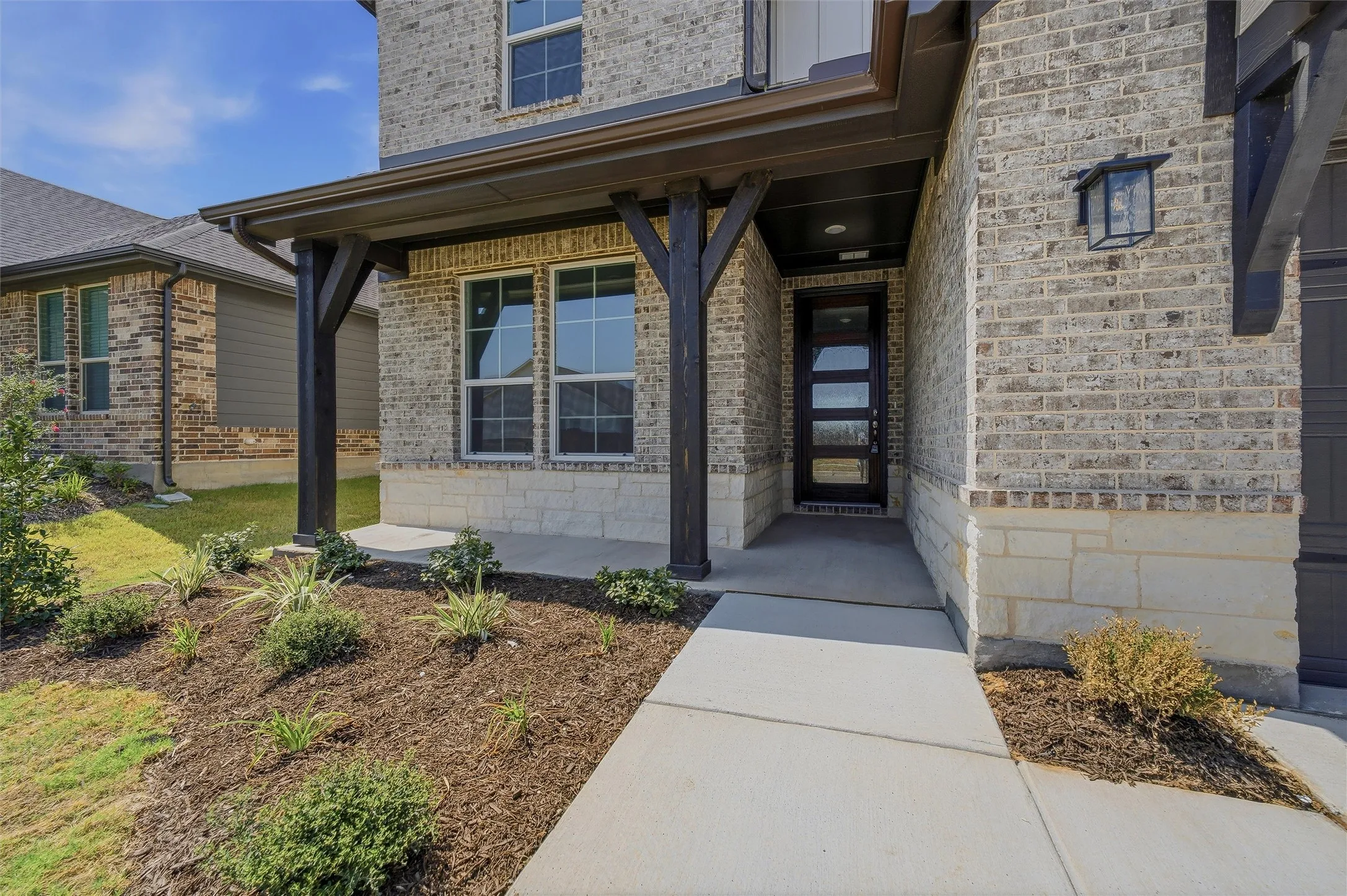 Brick and stone veneer exterior with a covered entry, dark-stained support columns, modern entry door, and exterior lighting fixture