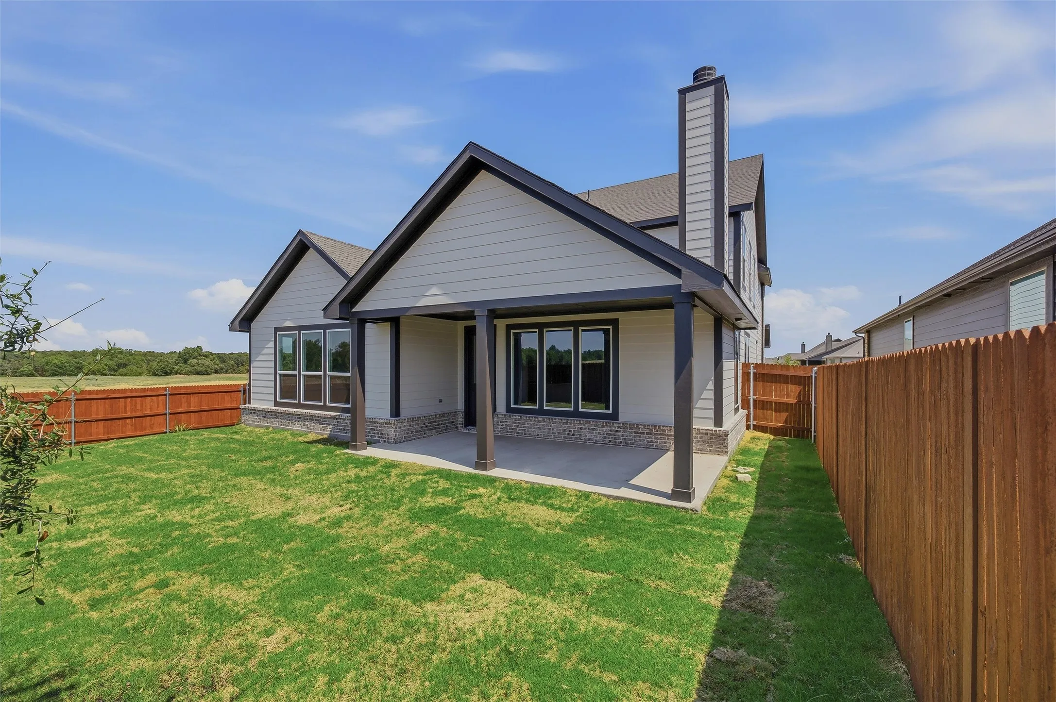 Expansive rear yard featuring a covered concrete patio, wood privacy fencing, and a stucco-clad chimney