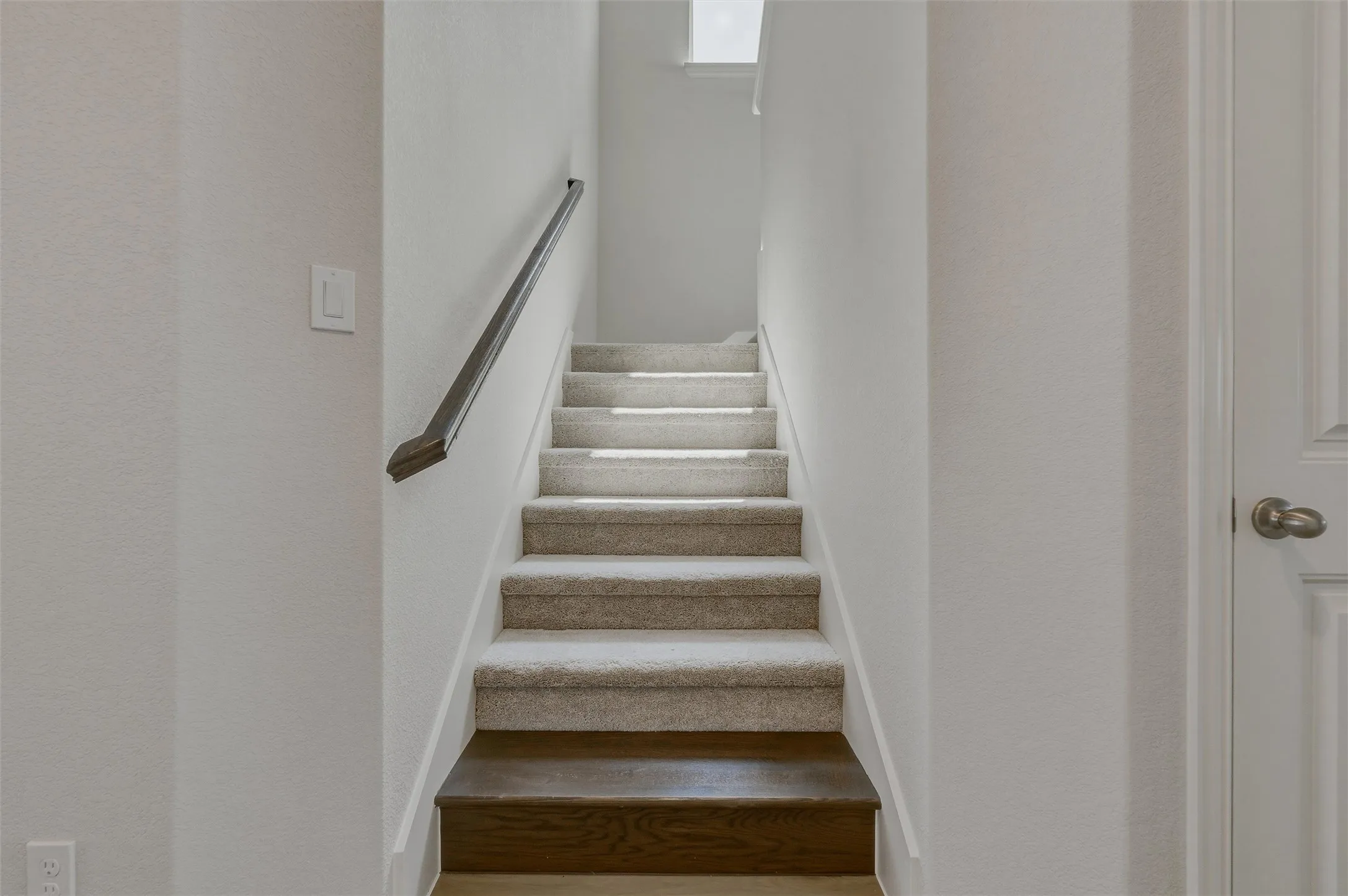 Staircase with carpeted treads, wood-finish risers, and a dark wood handrail