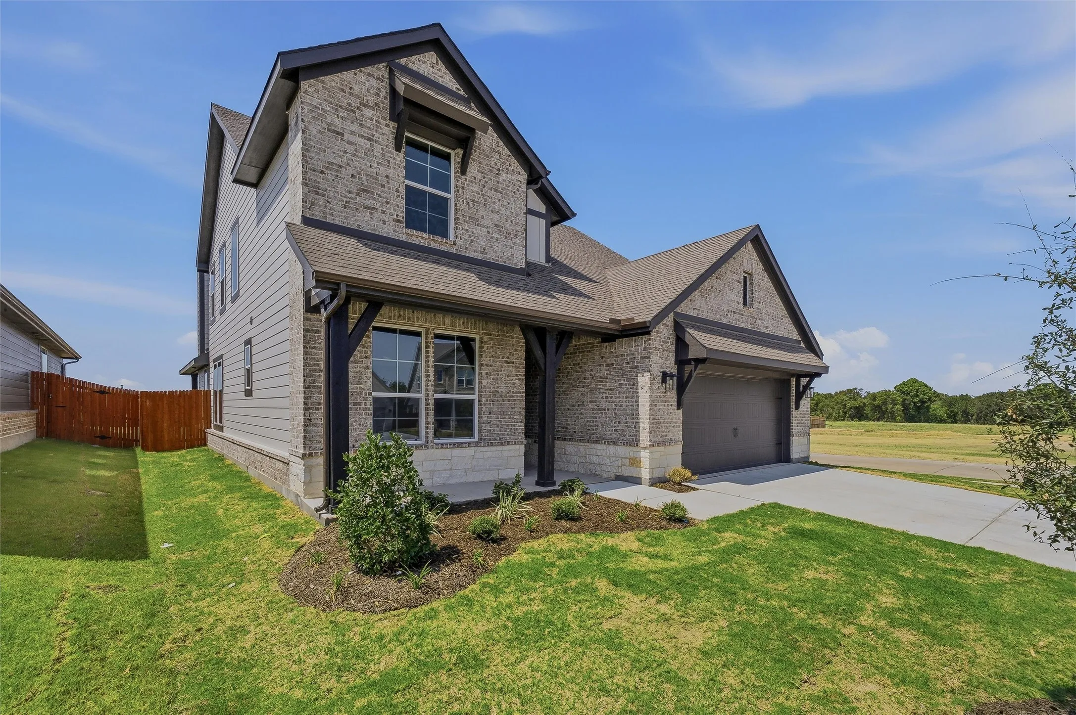 Brick and siding exterior with dark trim accents, covered entry, attached garage, and mature landscaping