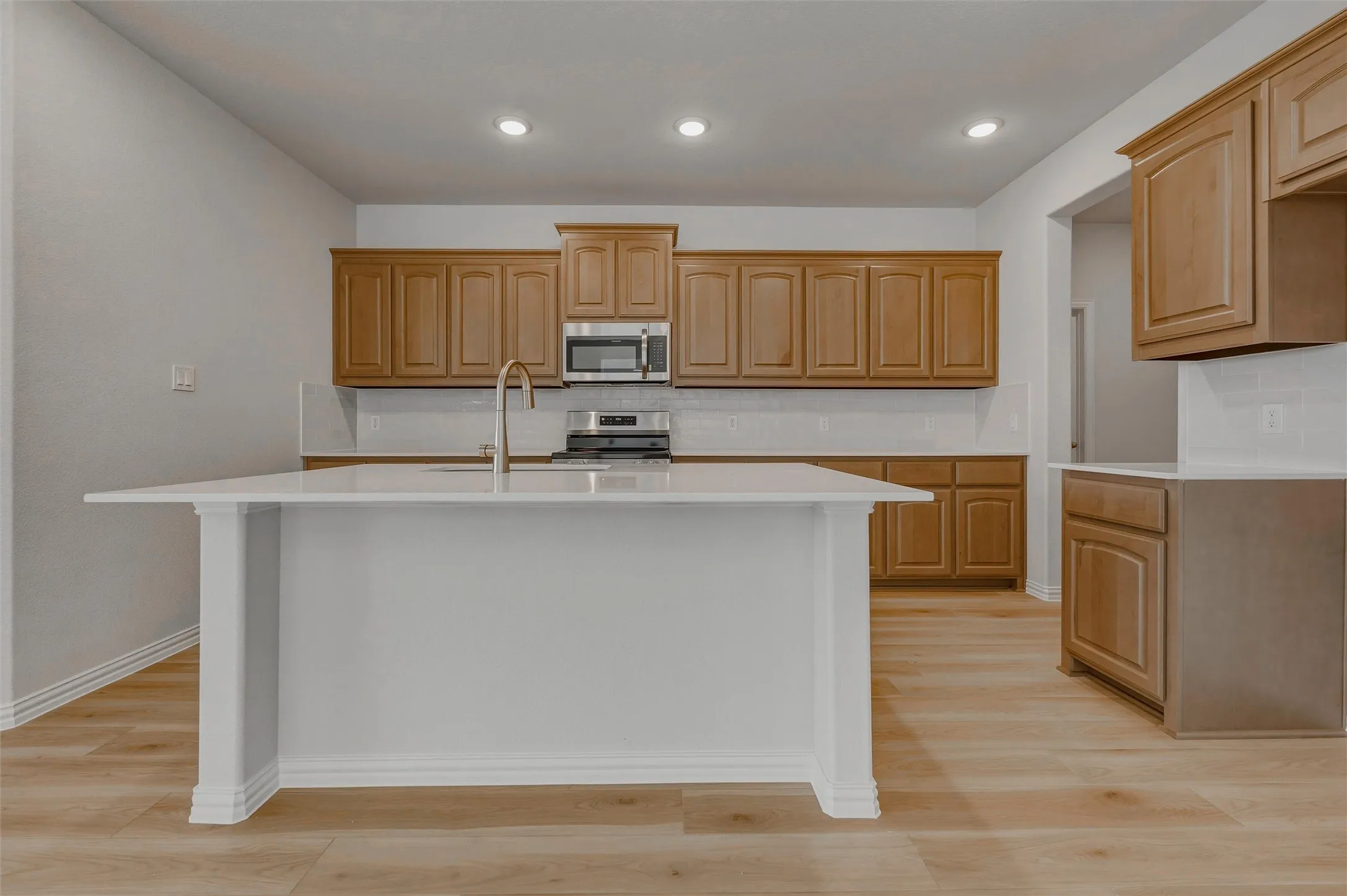 Kitchen featuring a center island with a sink, stainless steel appliances, wood-finish flooring, recessed lighting, and ample cabinetry