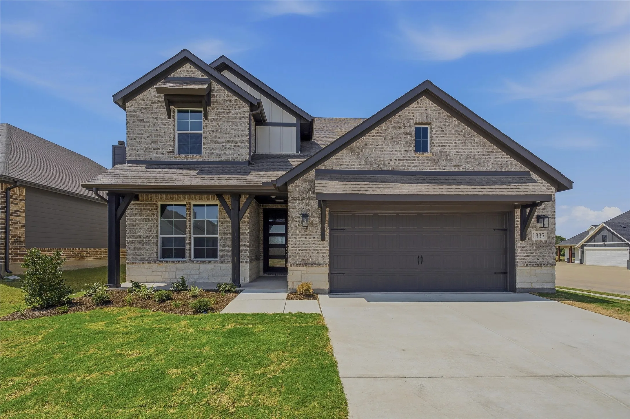 Brick and stone facade with dark trim accents, covered entry porch, dark garage door, and a concrete driveway