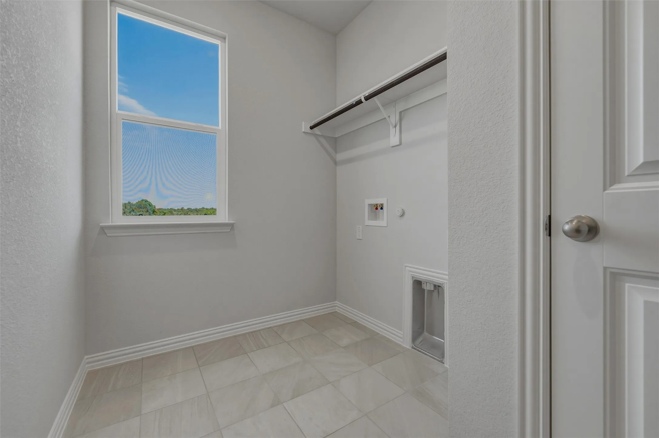 Utility room featuring a window, tile flooring, clothing rod, and appliance hookups
