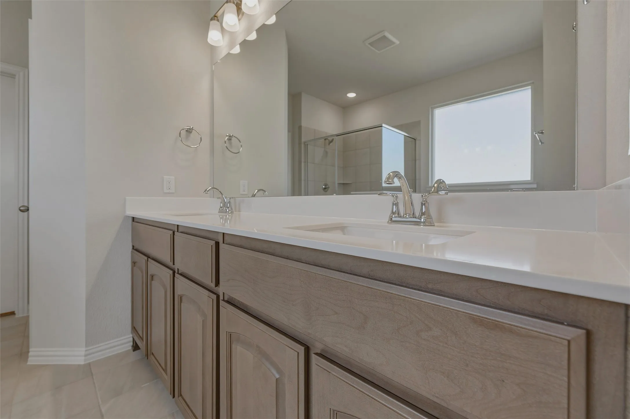Dual vanity with light wood-finish cabinetry, white countertop, and chrome fixtures