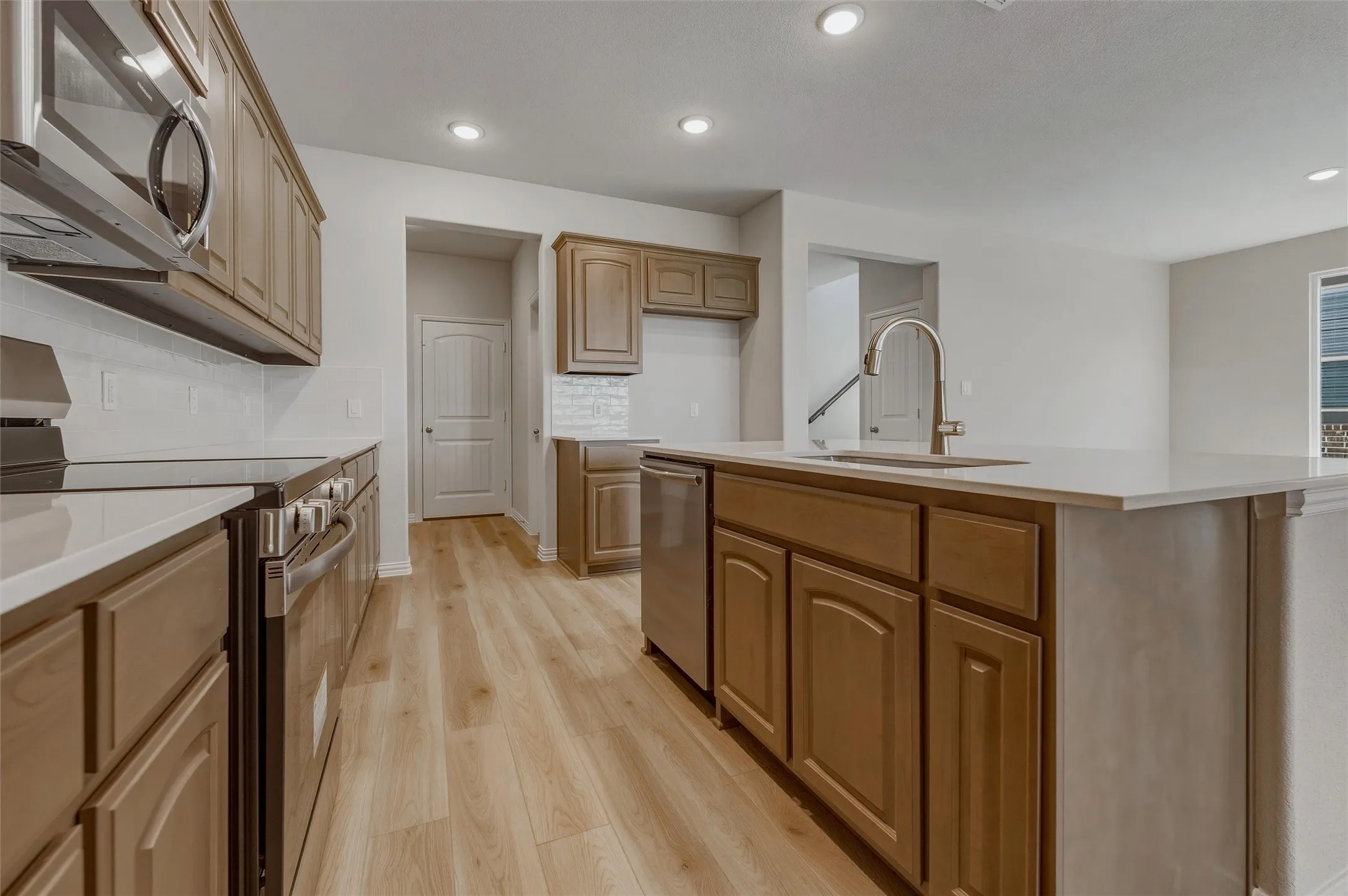 Kitchen featuring wood-finish cabinetry, stainless steel appliances, white countertops, and a large island with an integrated sink