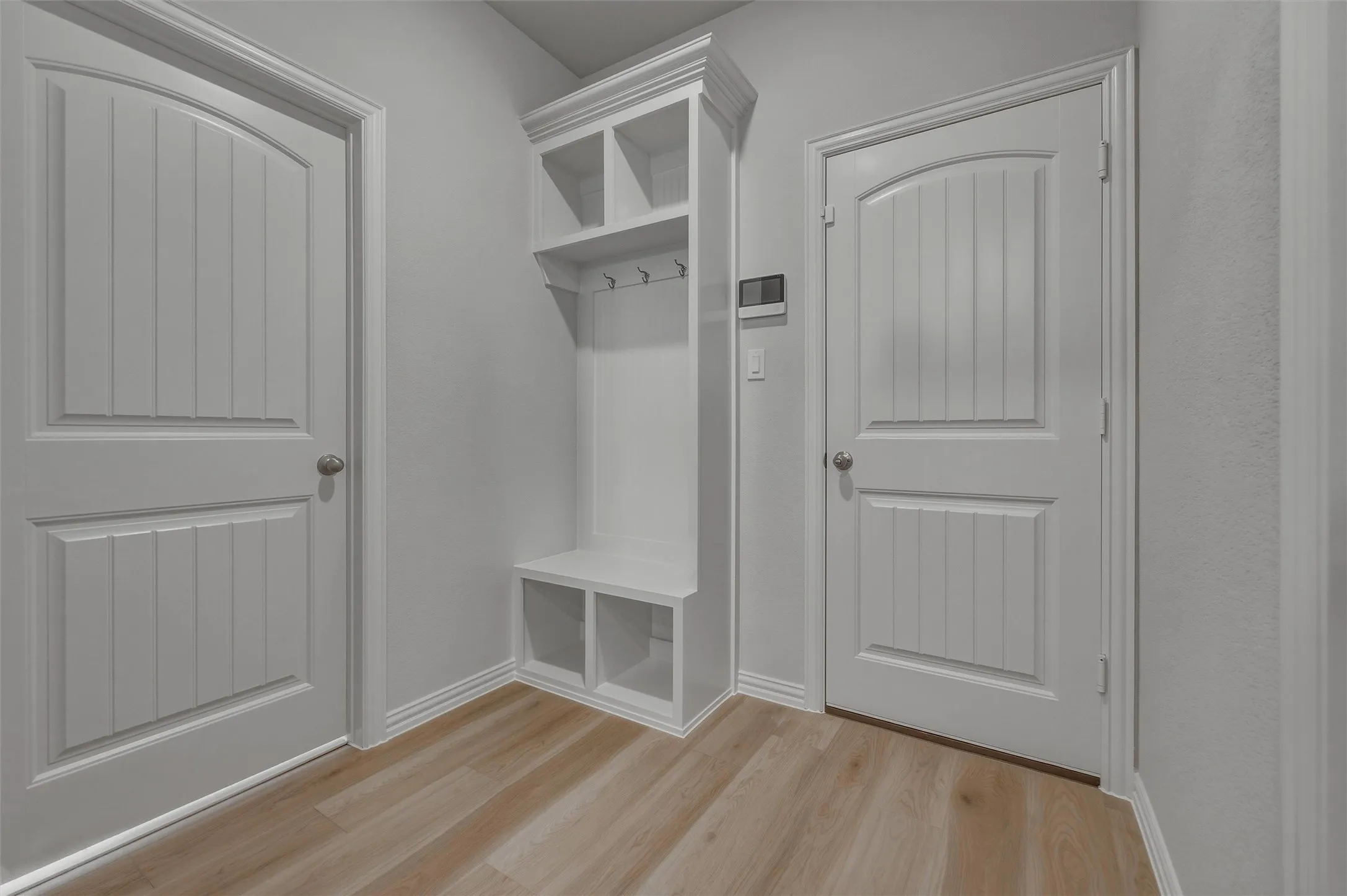 Built-in mudroom bench with cubby storage and upper shelving, wood-finish flooring, white paneled doors, and contemporary wall color