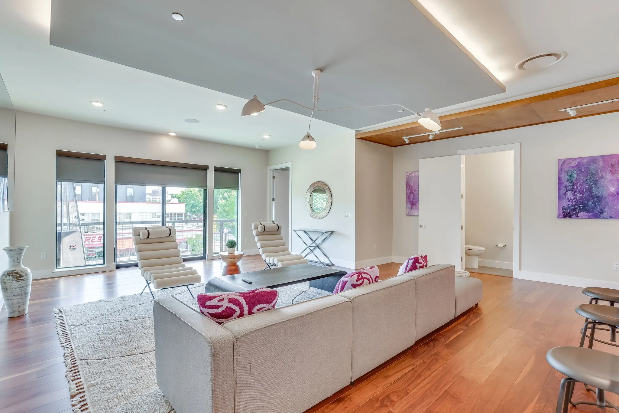 Spacious living area featuring Carlisle Wide Wood plank flooring, a contemporary ceiling design with integrated lighting, and large windows with shades