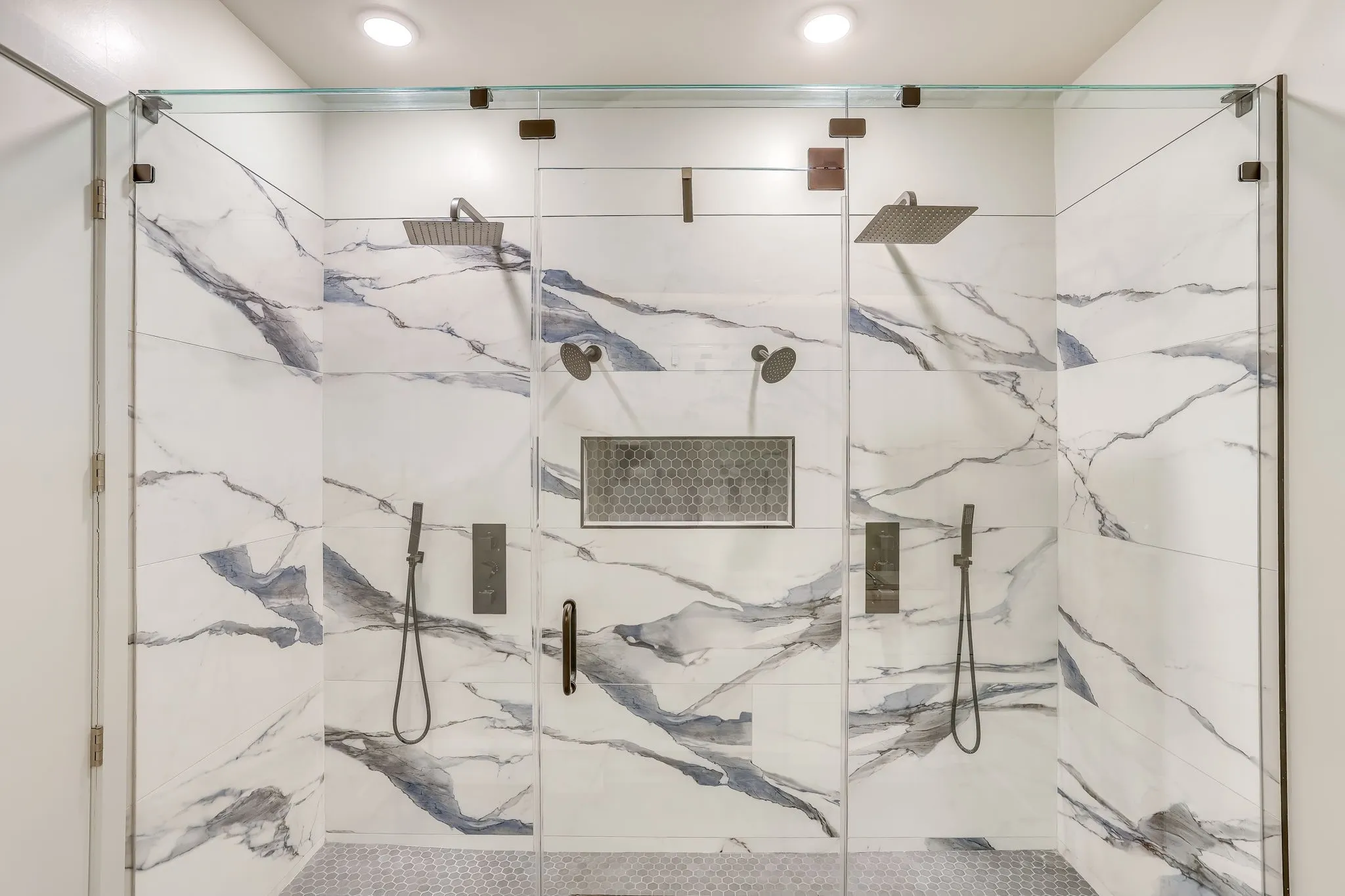 Remodeled Spacious shower featuring white and grey marbled tile and dual rain shower heads