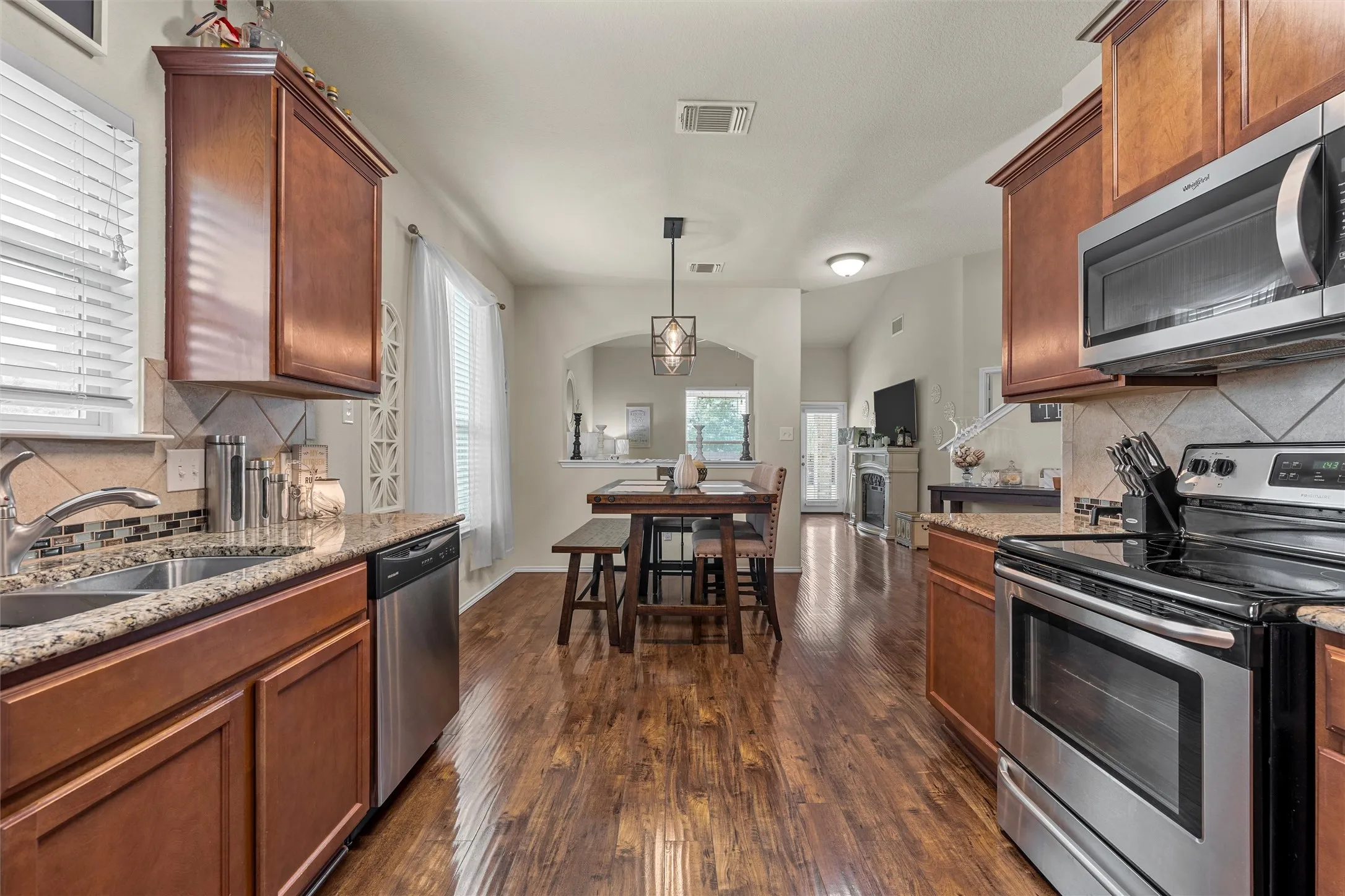 Open-concept kitchen featuring stainless steel appliances, wood-finish flooring, granite countertops, and wood cabinetry