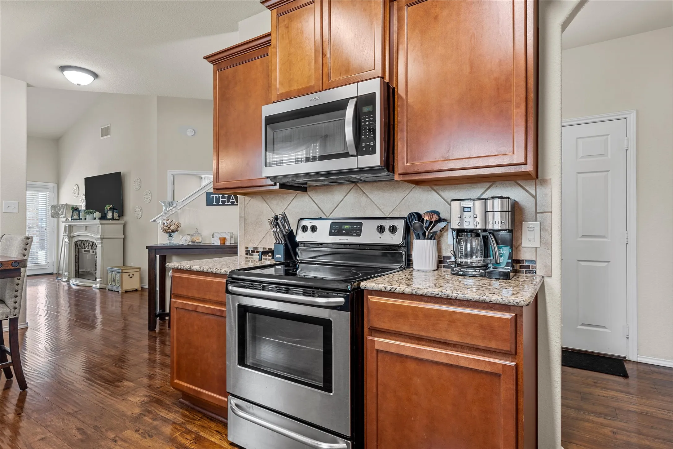 Kitchen featuring stainless steel appliances, wood-finish cabinetry, granite-style countertops, and a tile backsplash