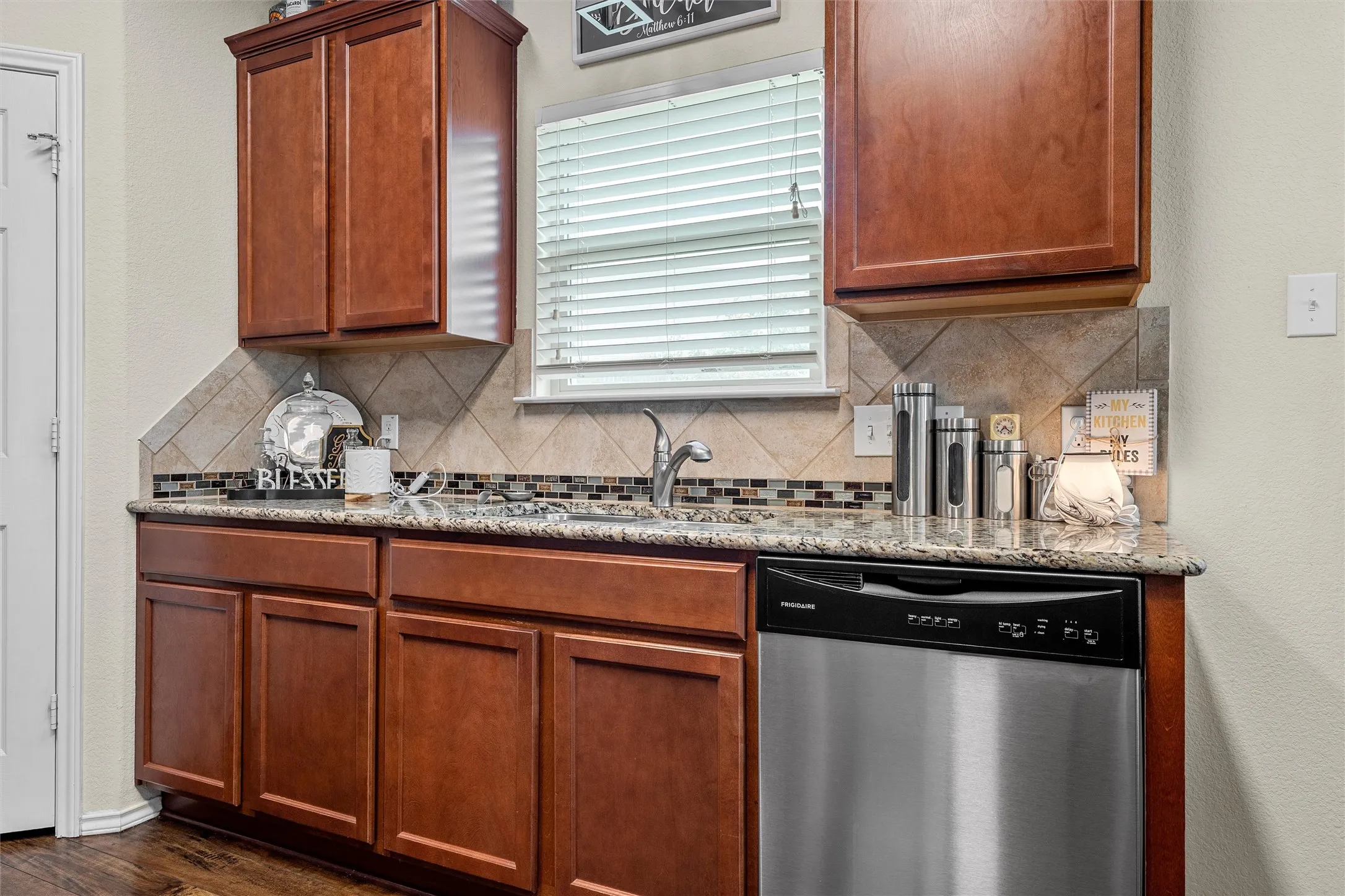 Kitchen countertop featuring wood cabinetry, a stainless steel dishwasher, and a stone-finish backsplash
