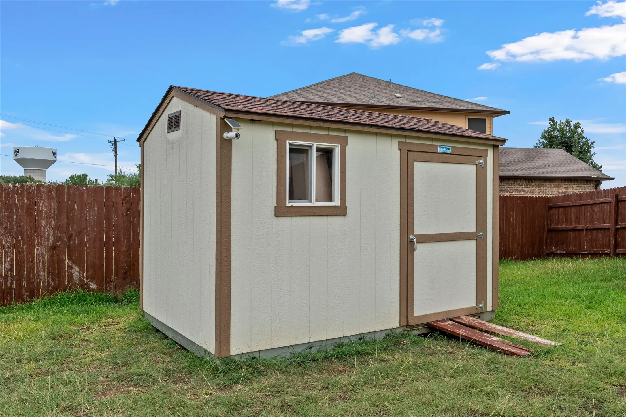 Detached storage shed featuring a single window, a single door, and a brown shingle roof