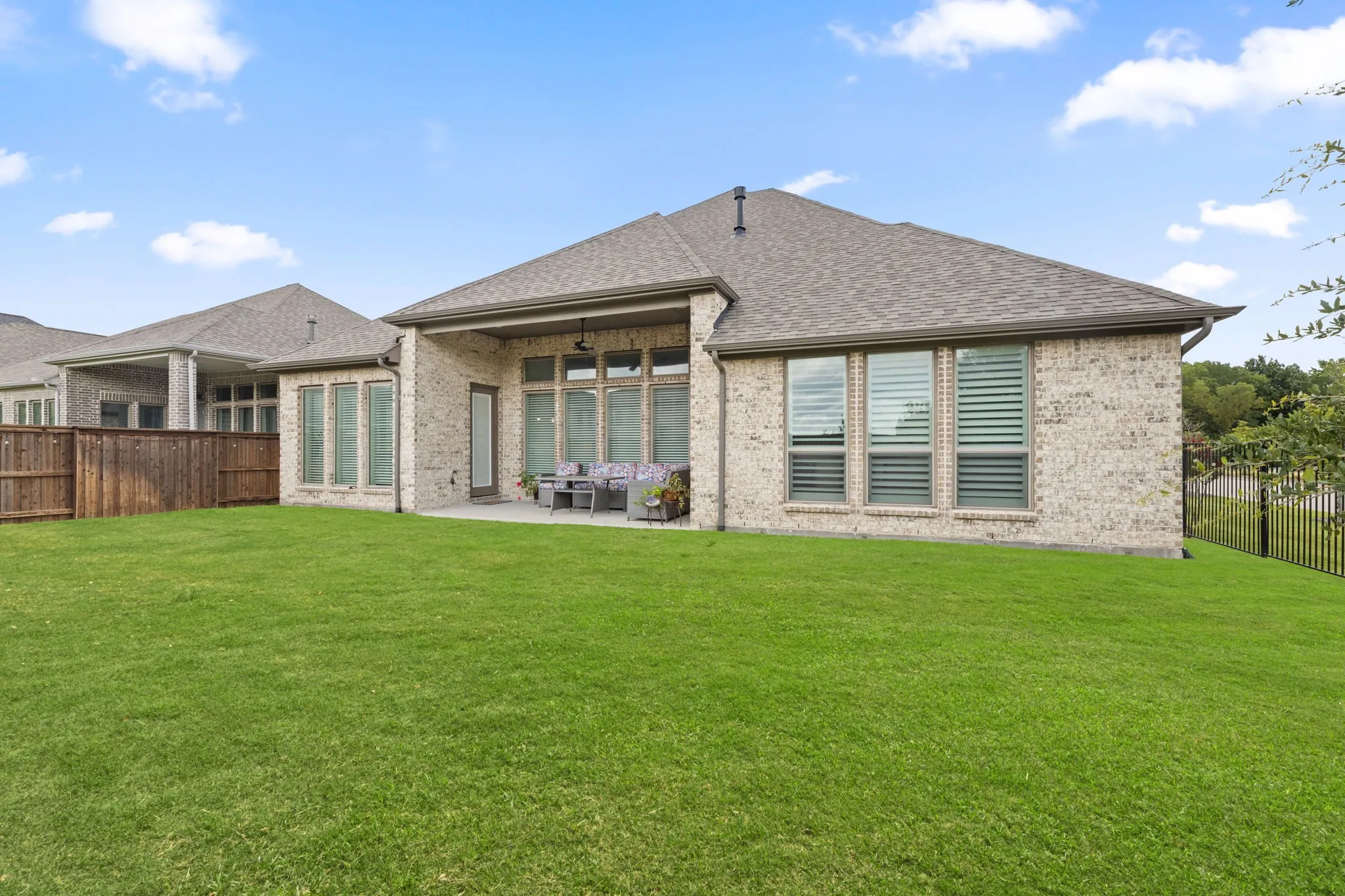 Spacious backyard featuring a covered patio, light-colored brick exterior, multiple large windows, and a dark shingle roof