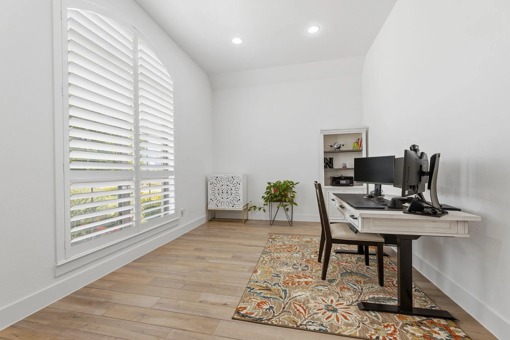 Room featuring an arched window with louvered shutters, light wood-finish flooring, recessed lighting, and white baseboards