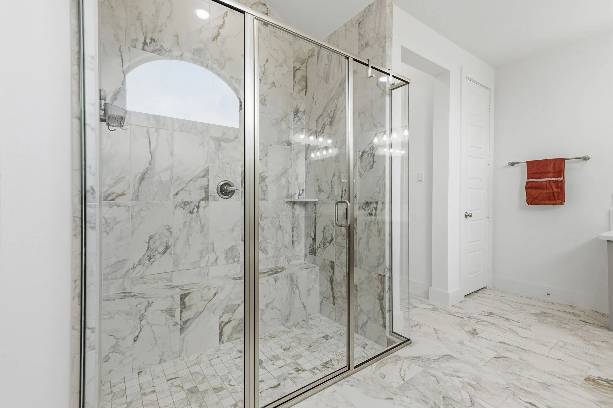 Glass-enclosed shower featuring large format wall and floor tiling, an arched transom window, a built-in bench, and a recessed shower niche